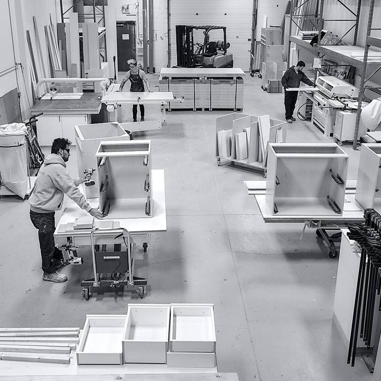 a black and white photo inside a cabinet making warehouse where 3 people are working on various cabinets