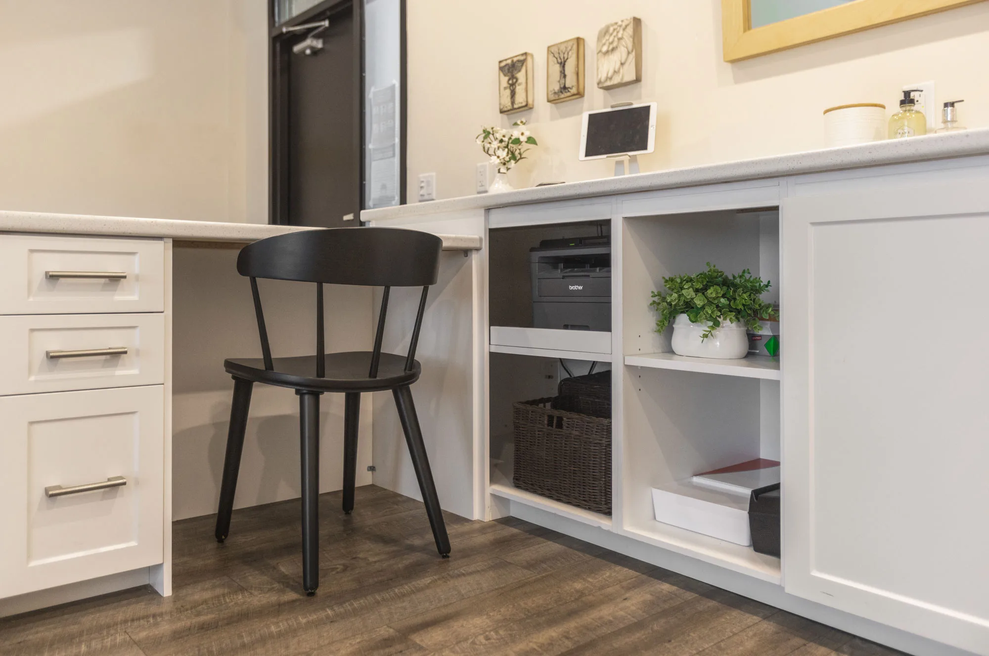 A close up of the back of a white cupboard reception area with a black chair and lower cupboards to store a printer and paper.