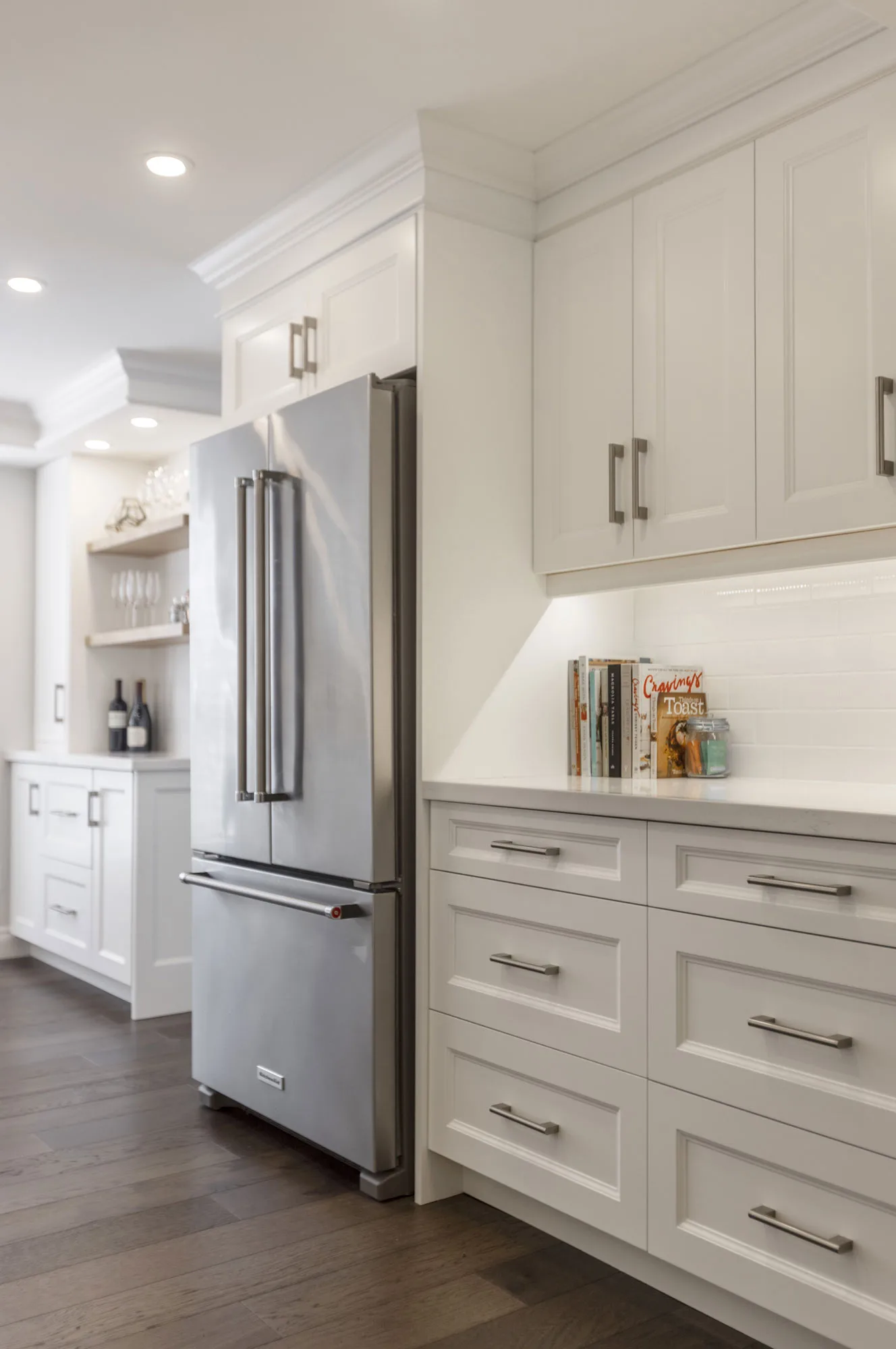 A kitchen with white cupboards with silver handles with a stainless steel fridge
