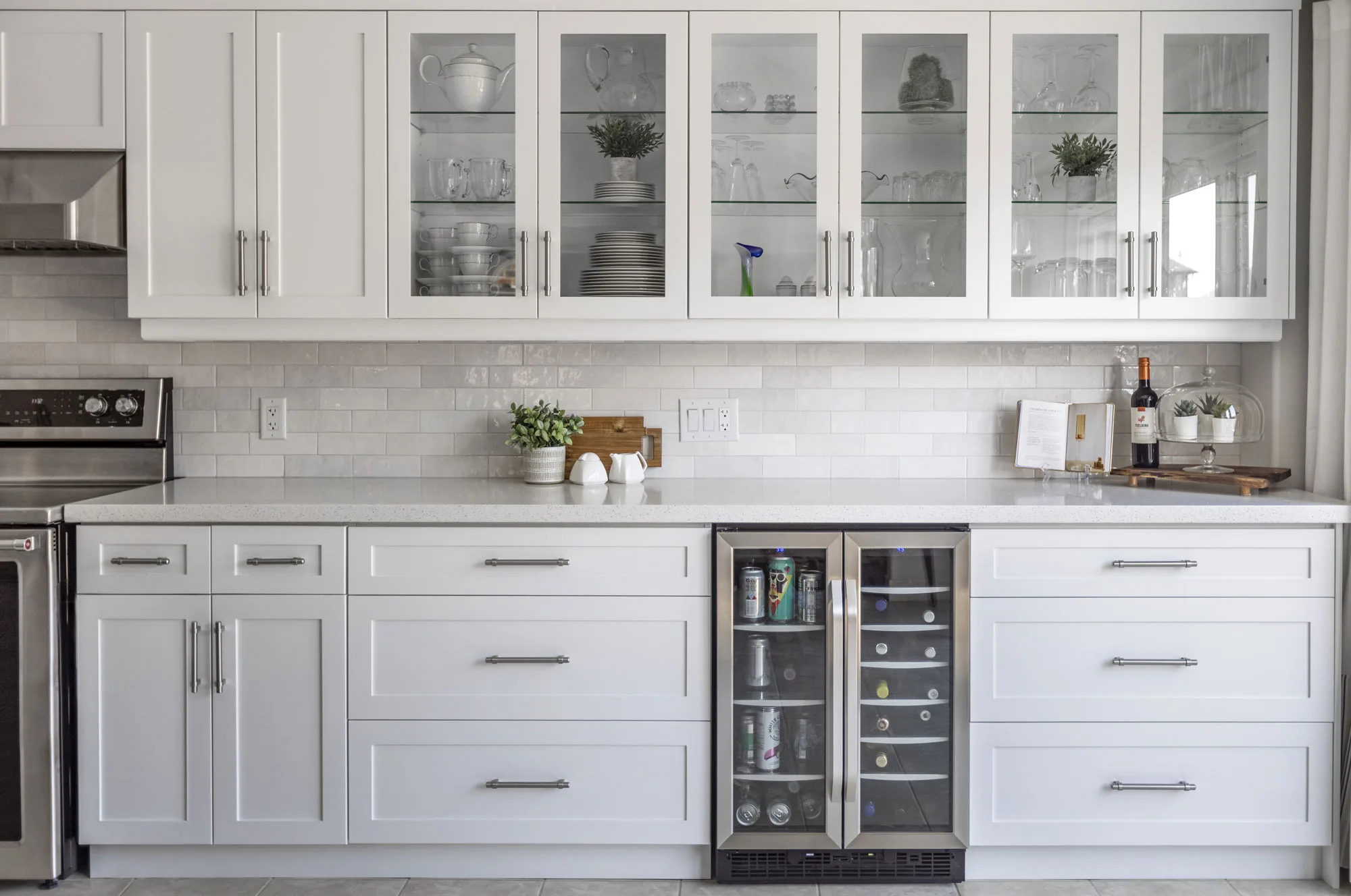 A modern white kitchen with glass top cupboards and a small stainless steel drink fridge.