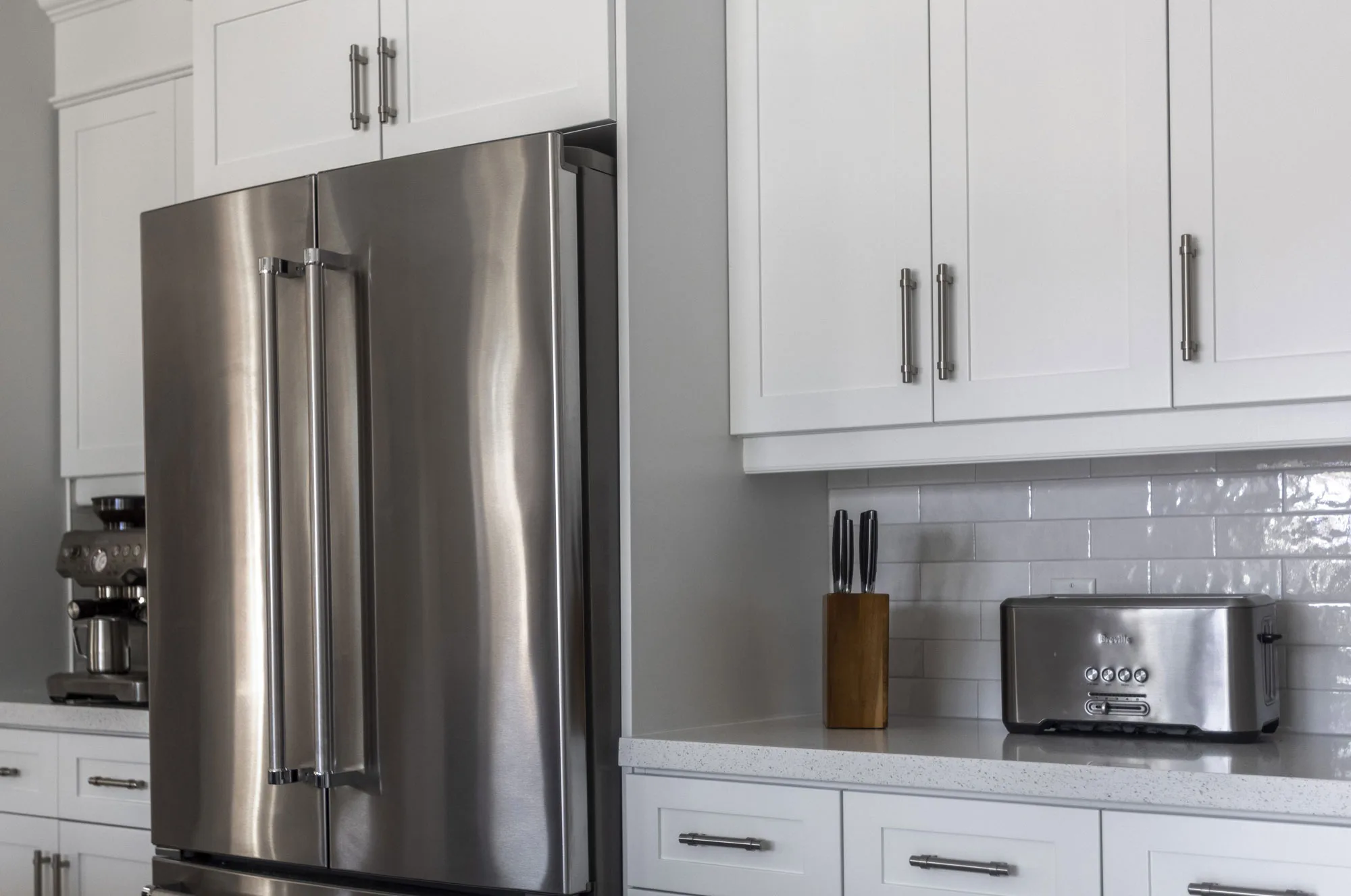 a close up of a stainless steel fridge and white cabinetry with silver handles with white subway tile backsplash