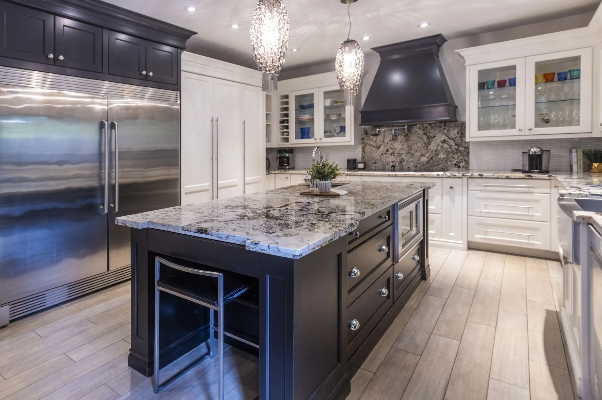 A kitchen with white cabinets and grey and black speckled granite counter top and back splash. Mixed with Dark blue cabinets with