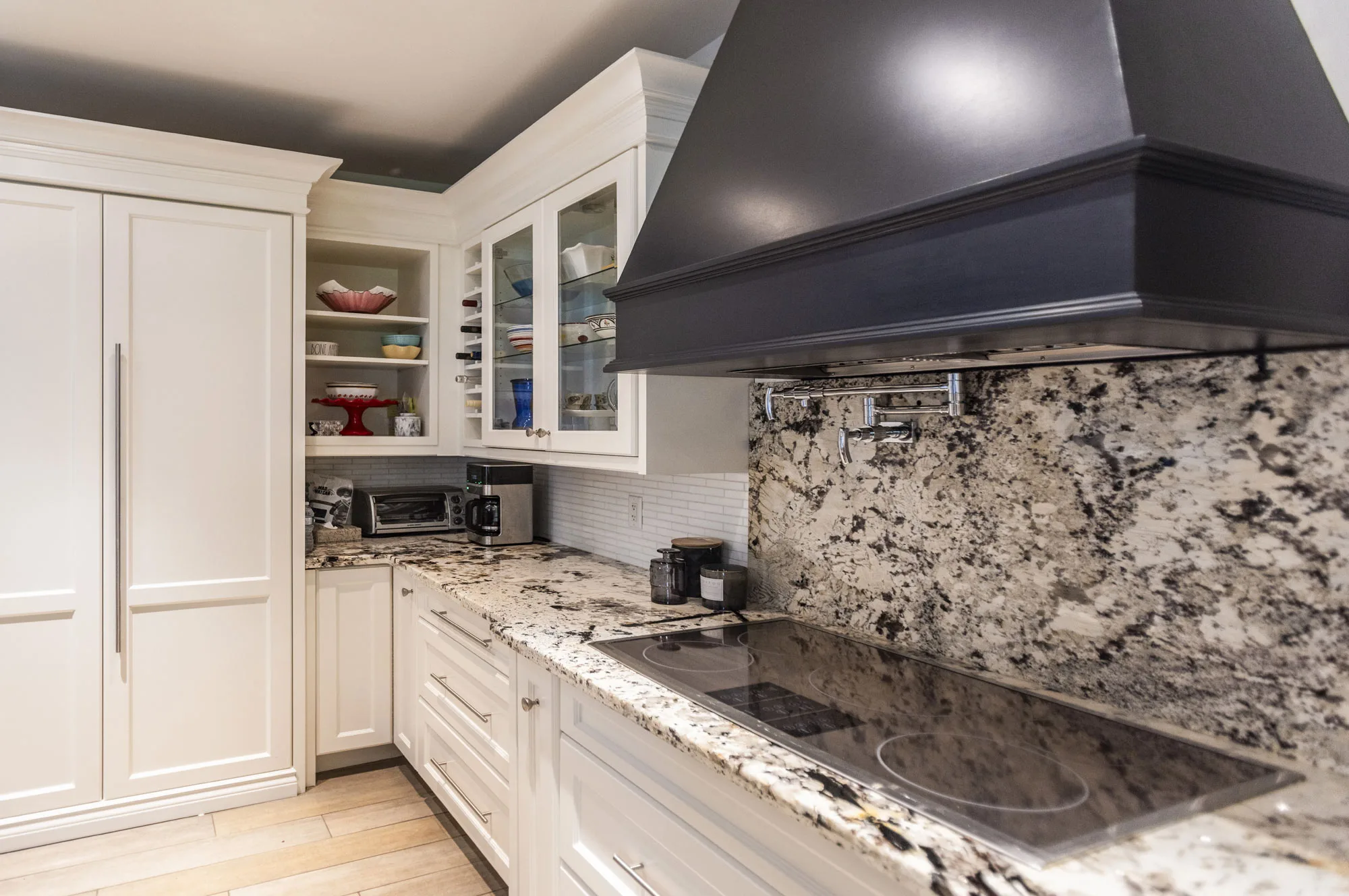 a close up of a side view of a kitchen with white cabinets and grey and black speckled granite counter top and back splash