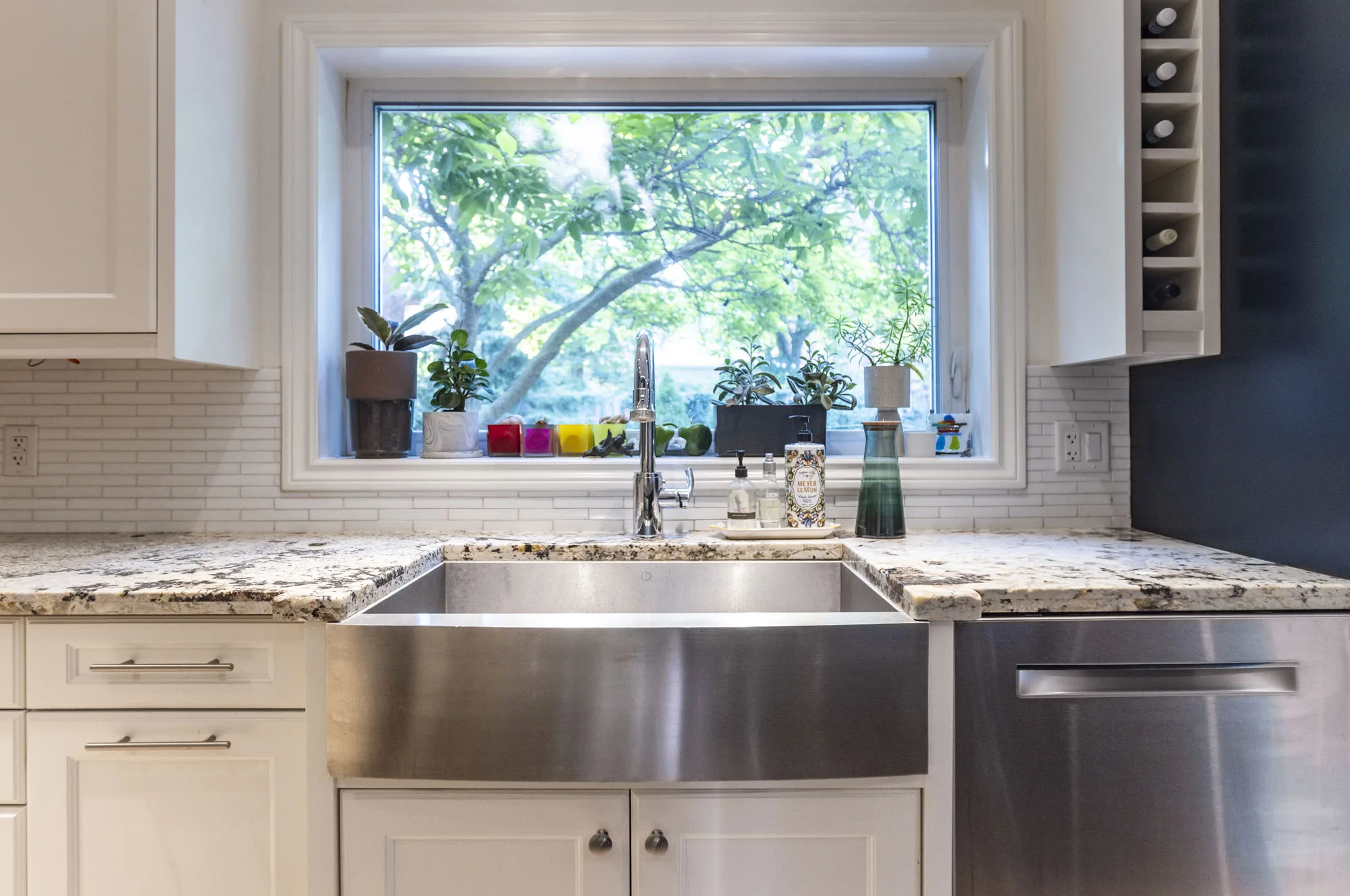 a kitchen with white cabinets with a stainless steel sink with a window above the sink