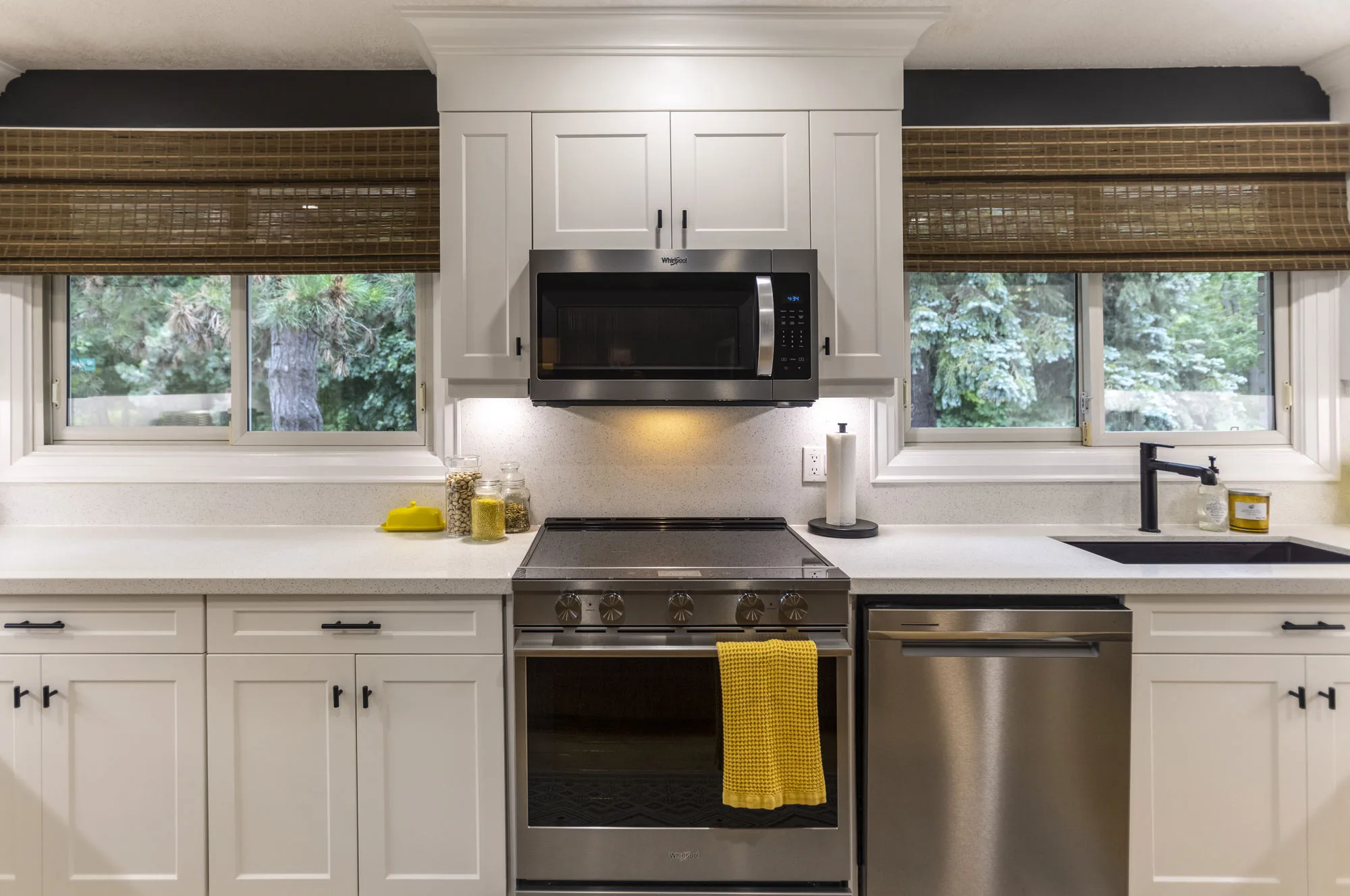 A modern kitchen cabinetry with black handles and stainless steel stove, dishwasher and microwave. A black sink with a black faucet