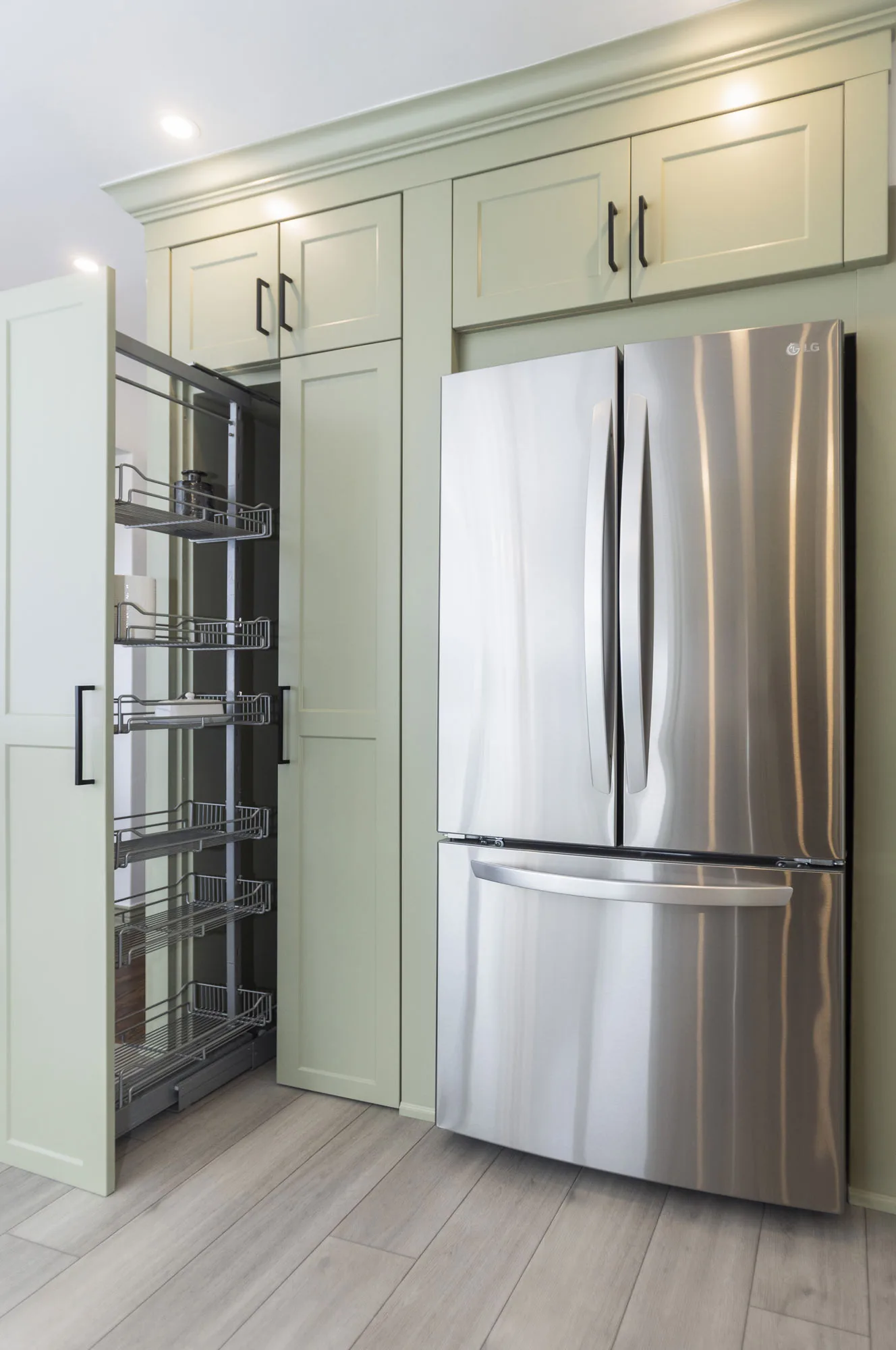 a close up of a light green kitchen with a stainless steel fridge and a pull out cupboard.