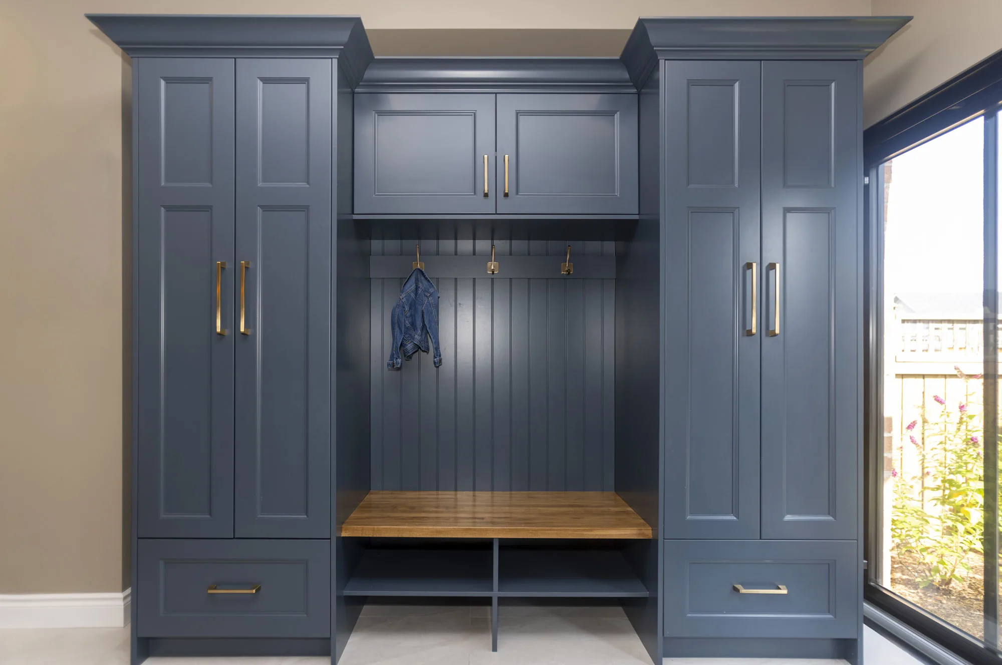 A dark blue custom built storage cabinets with gold handles and hooks