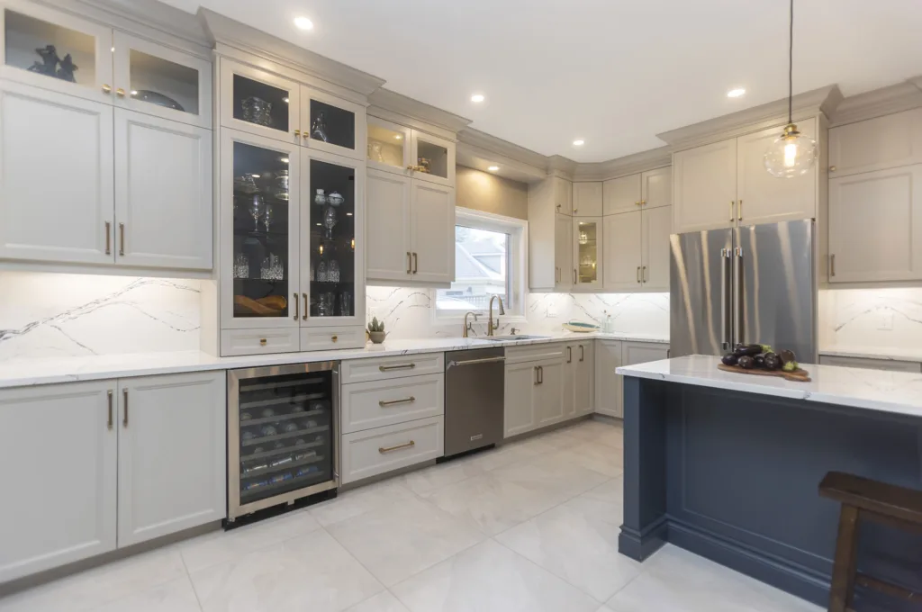 A modern kitchen with off-white cabinentry accented with gold handles along with a dark blue island with white counter tops and gold fixtures and stainless steel appliances