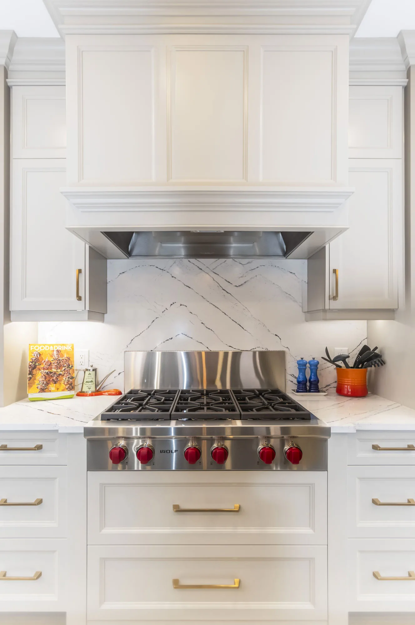 Close up of off-white cabinets and gold hardware with a gas stove top with red handles