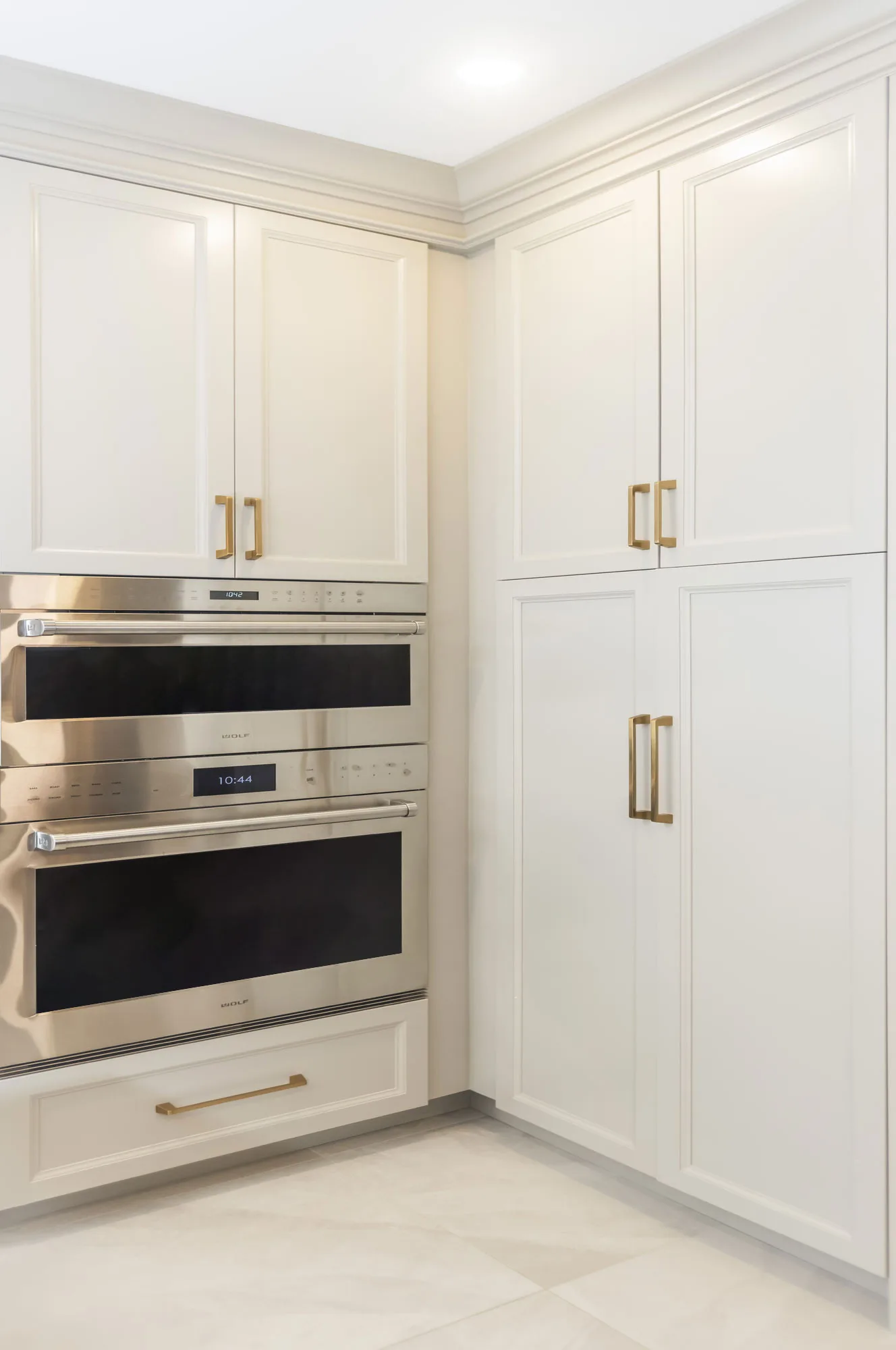 Close up of off-white cabinets and gold hardware with a built in double stainless steel oven