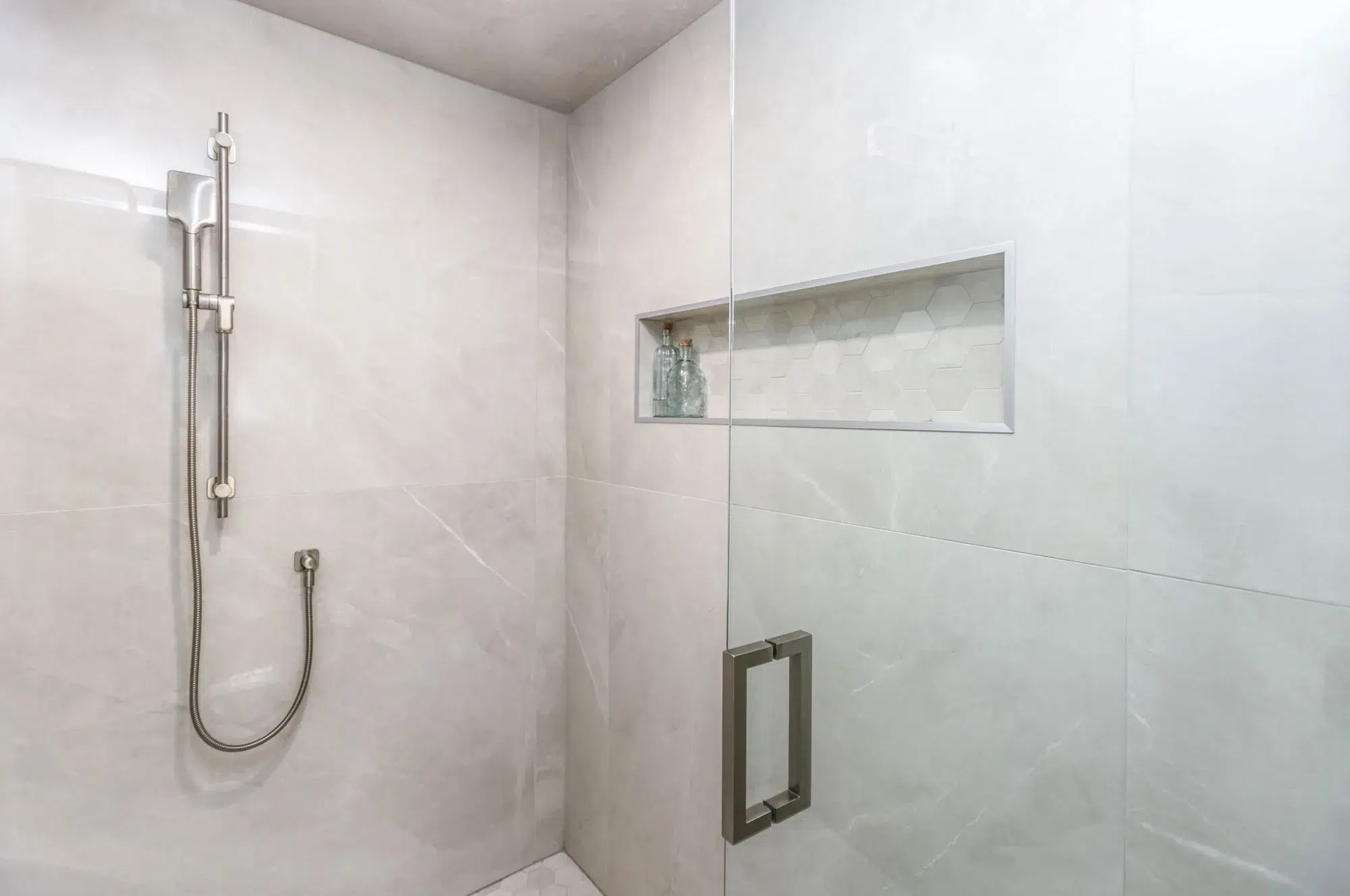 Inside a beautiful tiled shower with glass door with nickel hand held shower