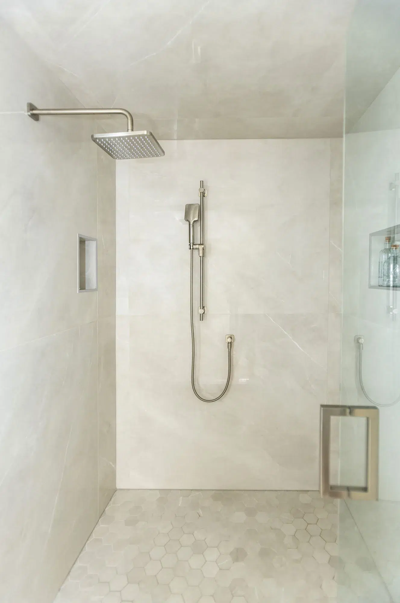 Inside a beautiful tiled shower with glass door with nickel rain shower head and hand held shower