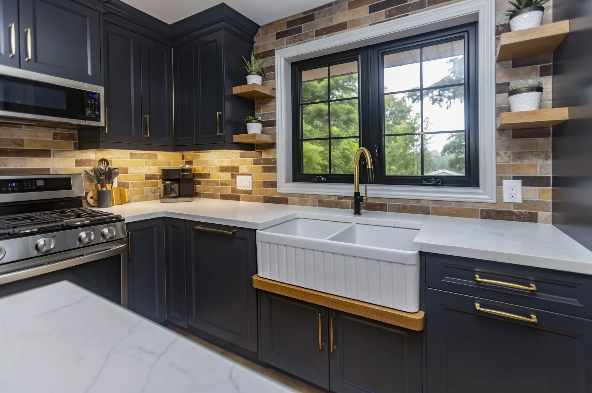 Kitchen with dark navy uppers and lowers with gold hardware and stainless steel appliances along with a deep white double sink with a gold tap