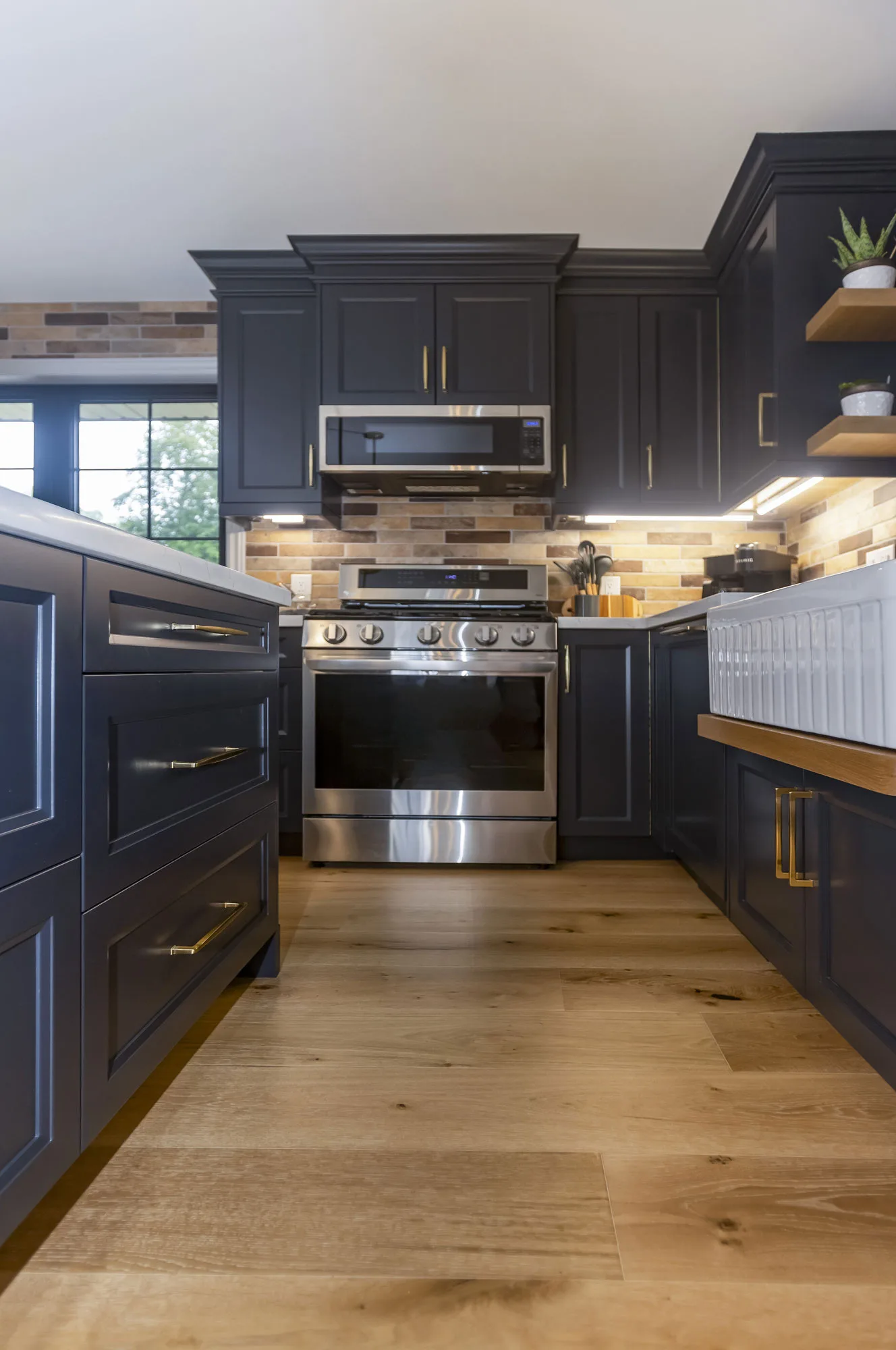 Kitchen with dark navy uppers and lowers with gold hardware and stainless steel appliances along with an island.