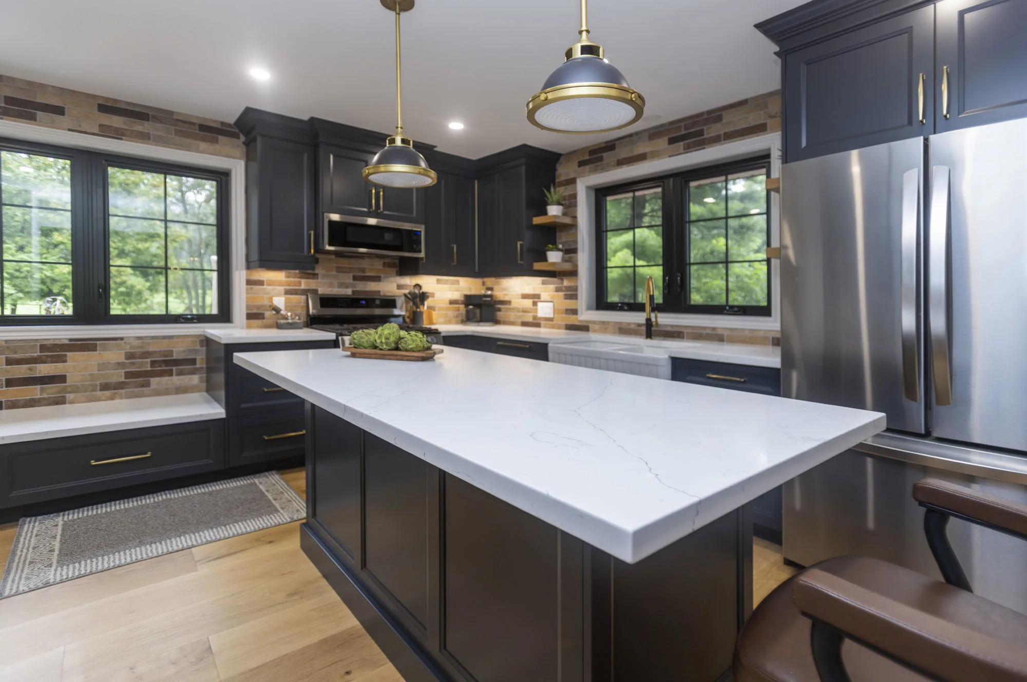 Kitchen with dark navy uppers and lowers with gold hardware and stainless steel appliances along with an island with vintage overhead lights