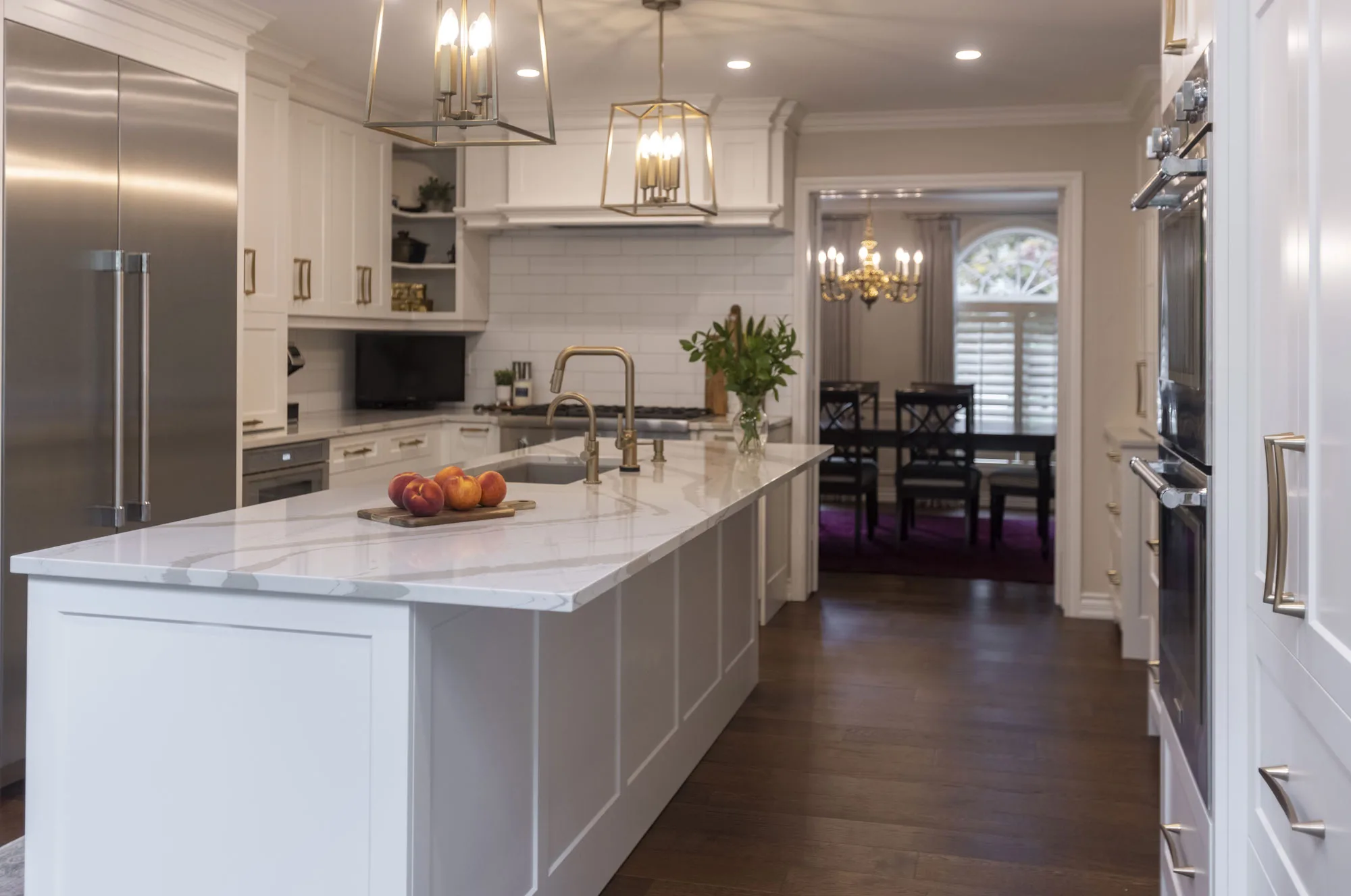 A large kitchen with white upper and lower cupboards with large silver handles and large white island.