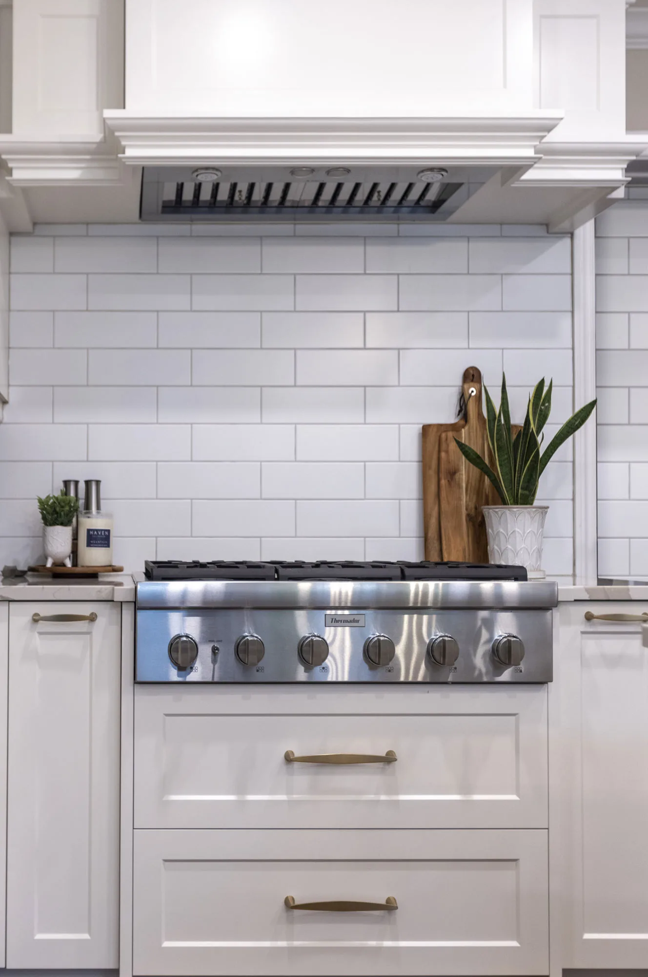 A close up of a modern white kitchen with large subway tile backsplash and stainless steel oven top