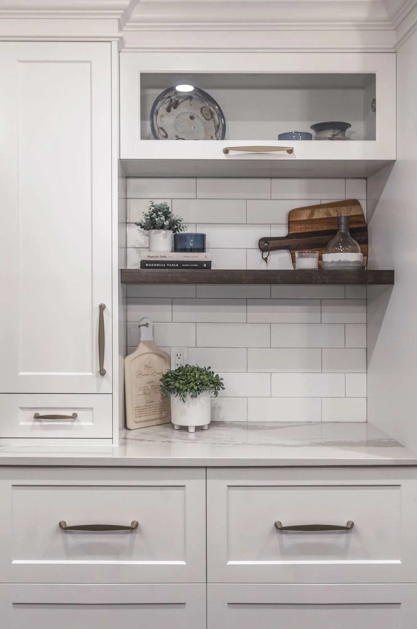 Close up of an area of white kitchen with silver handles with a dark wooden shelf