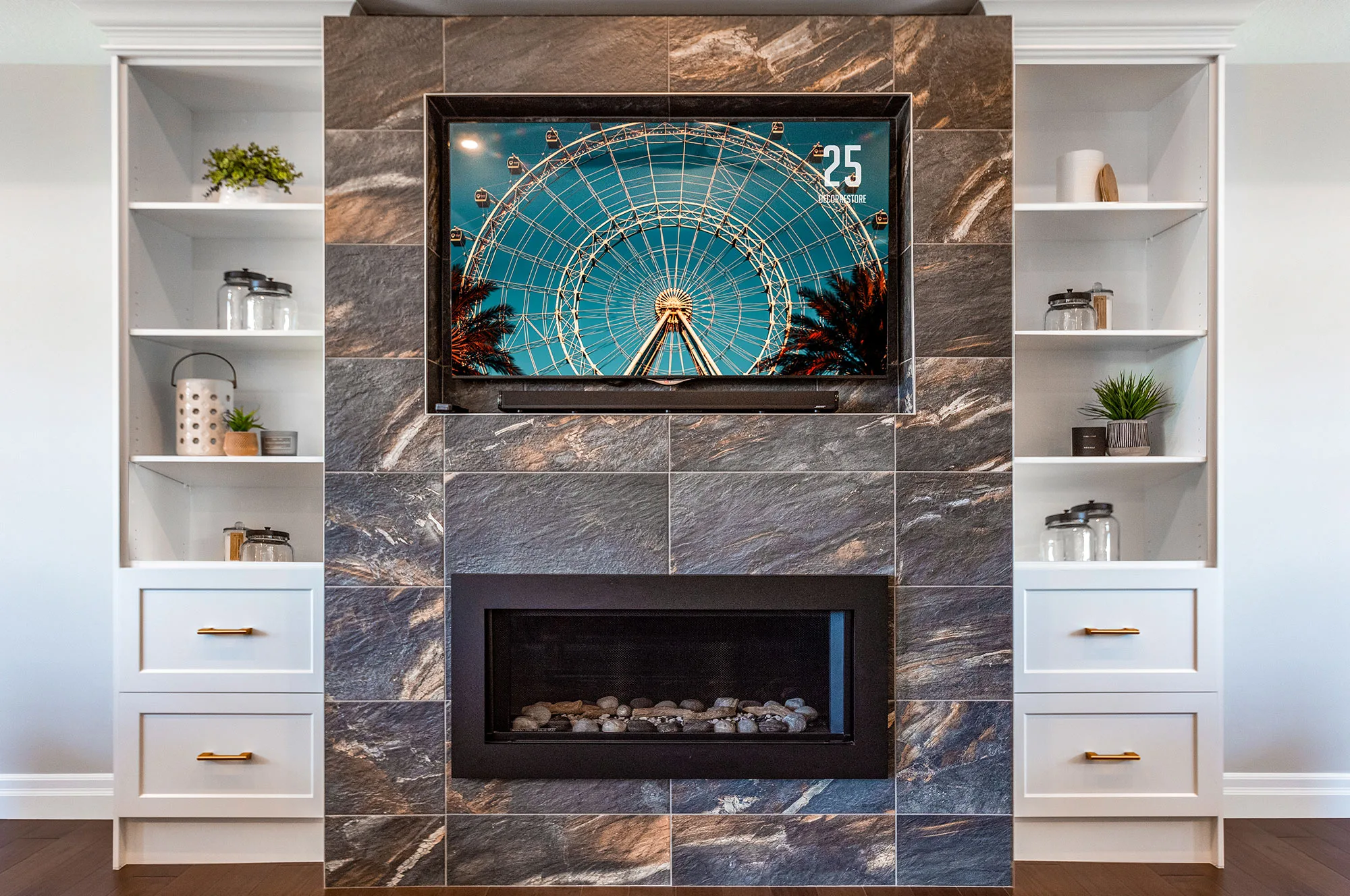 A fireplace with tv above surrounded by tile along with shelving drawers on either side