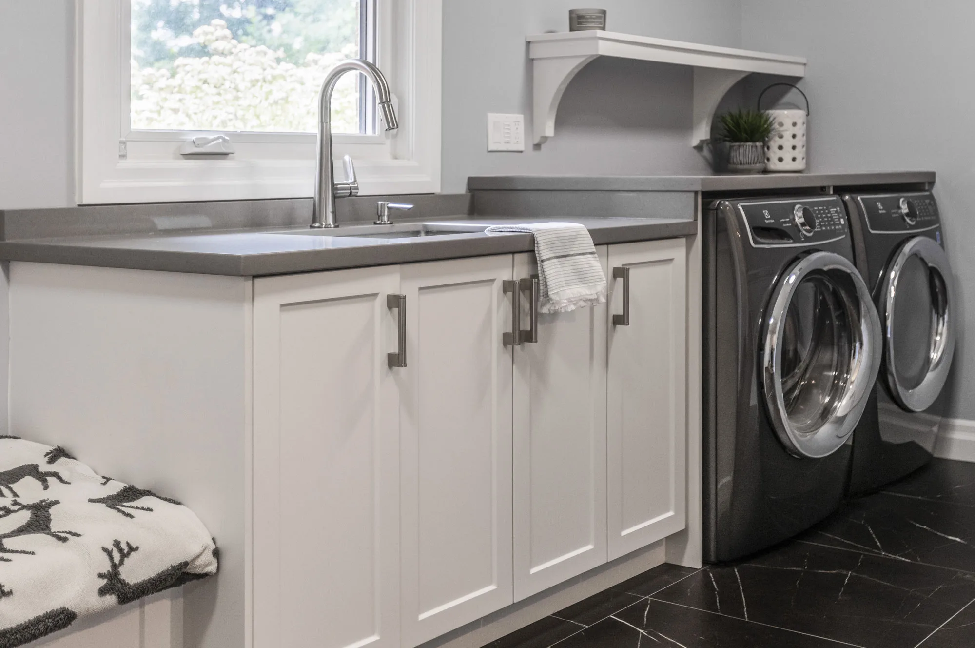 Close up of lower white cupboards with silver handlesand dark grey counters with a dark grey washer and dryer.