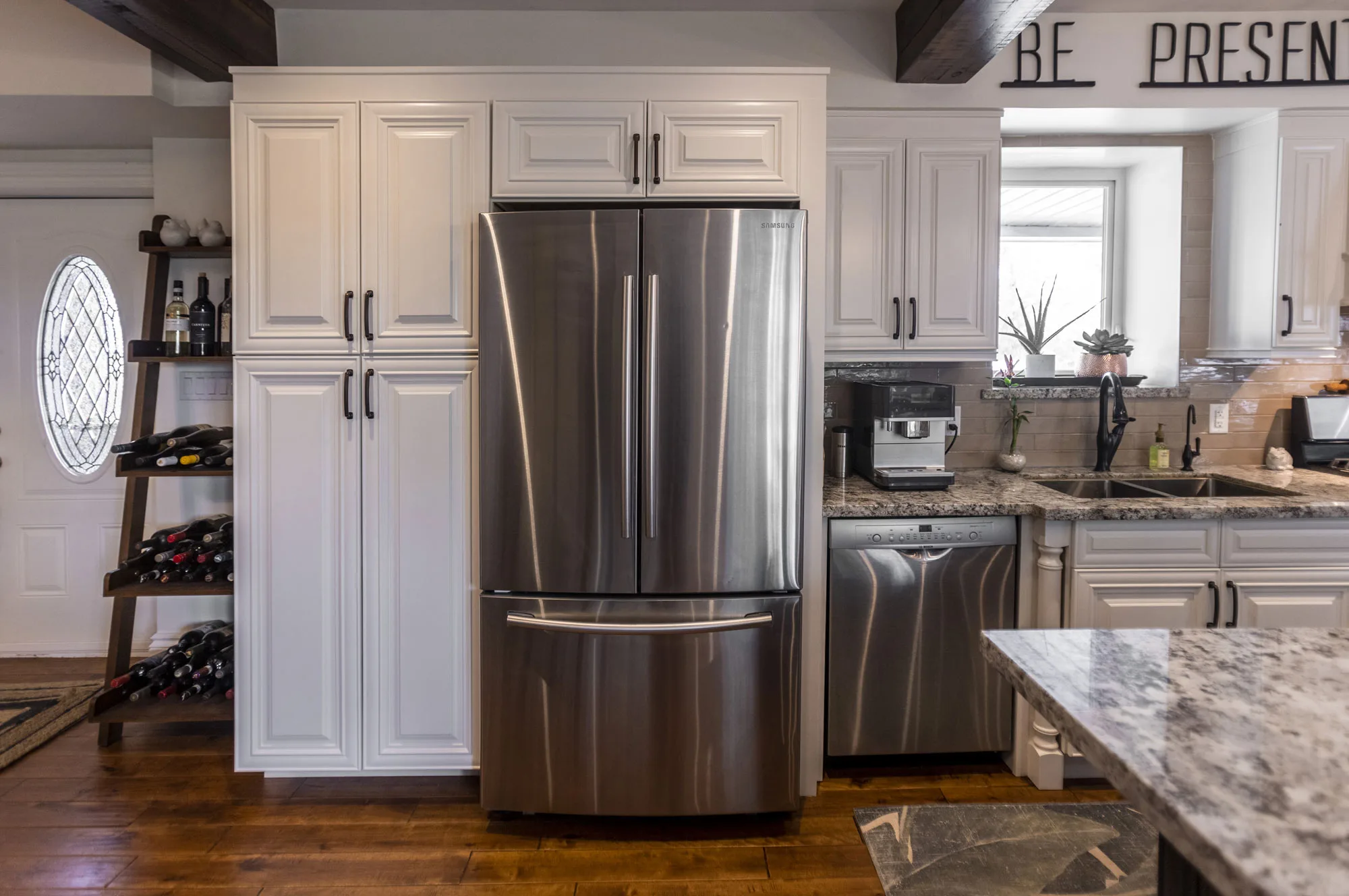 A beautiful white cupboards and black handles and stainless steel fridge and dishwasher.