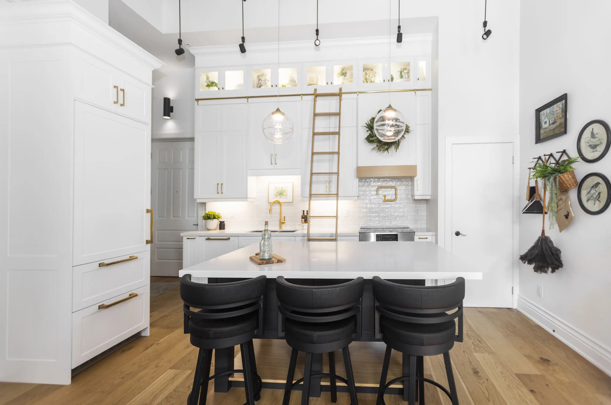 An all white modern kitchen with gold hardware with a gliding gold ladder with a breakfast bar