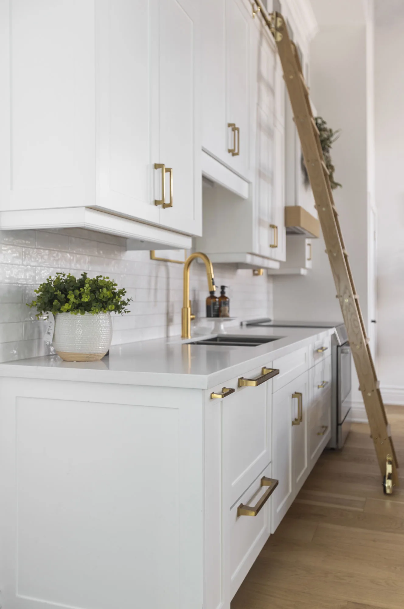 A side view of an all white modern kitchen with gold hardware with a gliding gold ladder