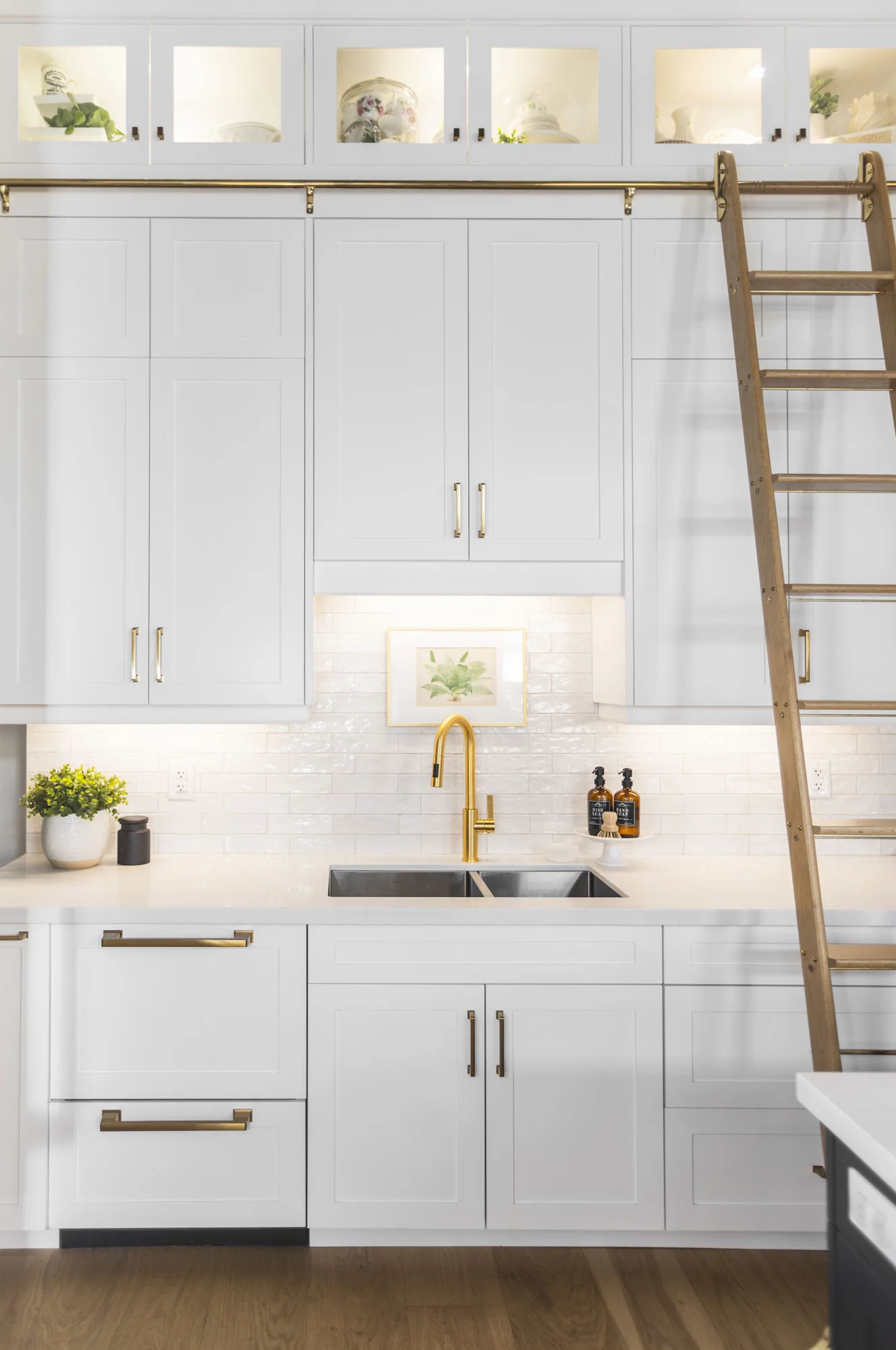 An all white modern kitchen with gold hardware with a gliding gold ladder