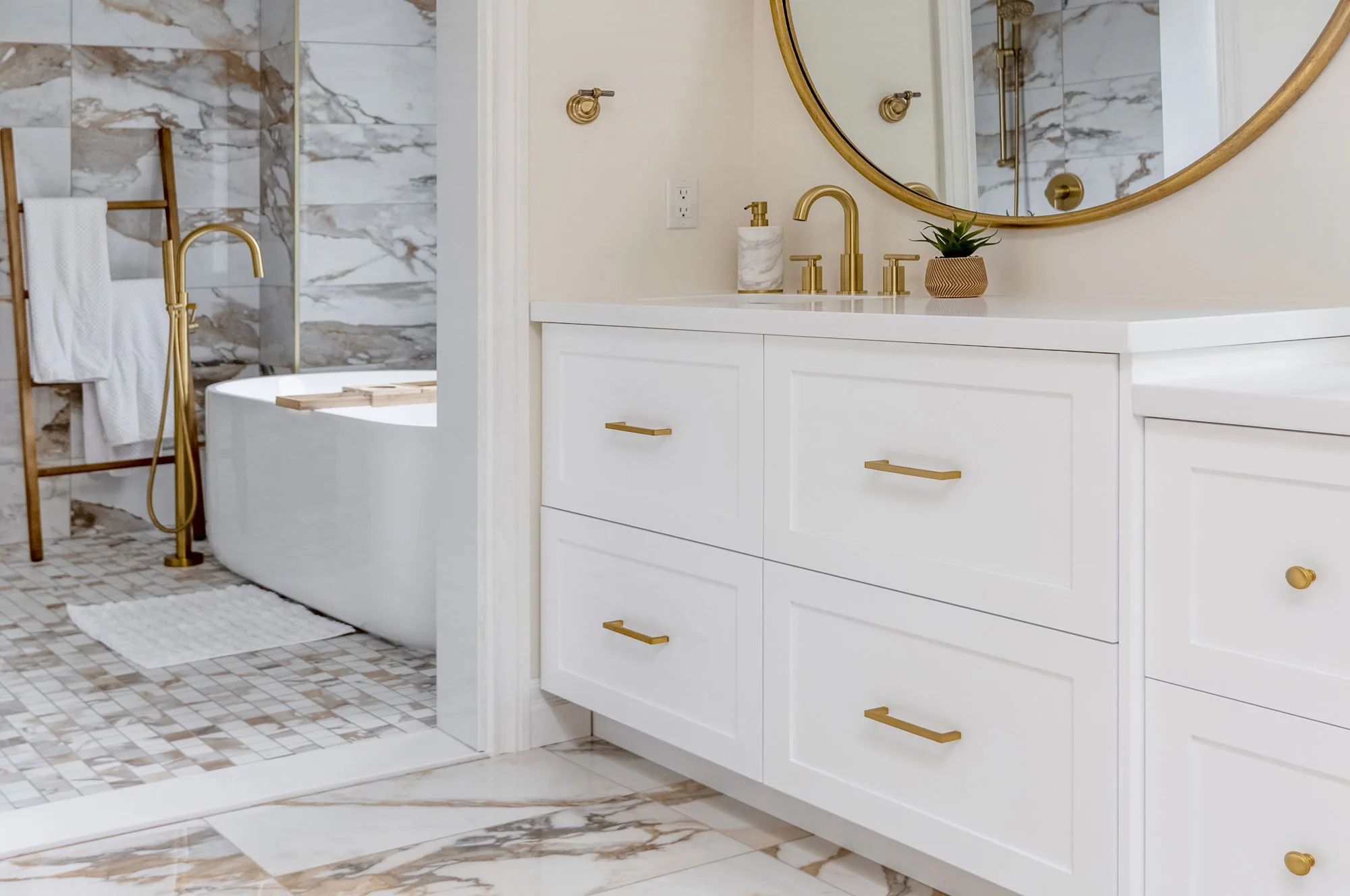 A close up of a white cupboard bathroom accented with gold handles and gold trimmed mirror along with gold faucets.