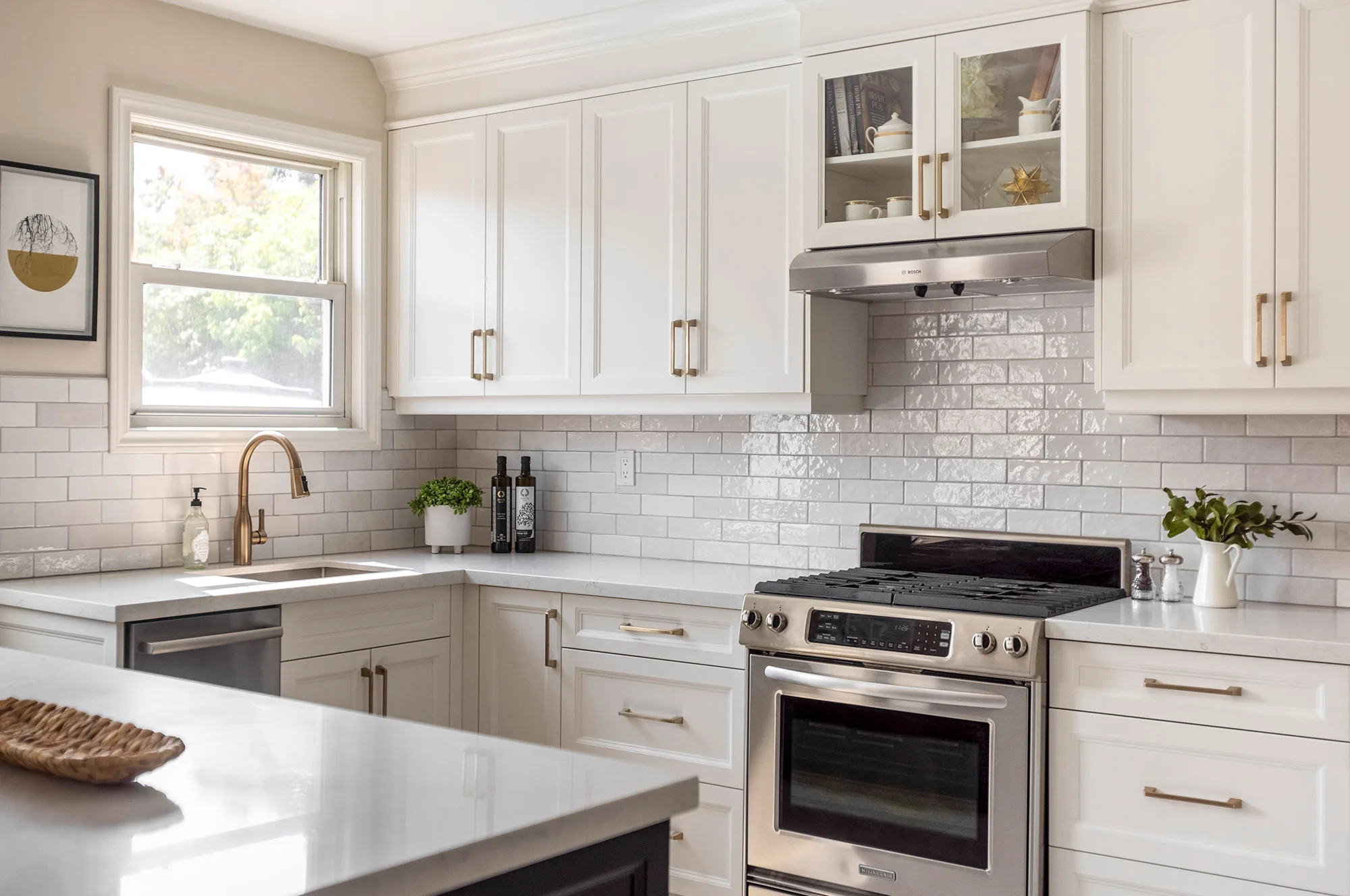A kitchen with white upper and lower cupboards with silver handles with a stainless steel oven and hood with white and light grey subway tile backsplash