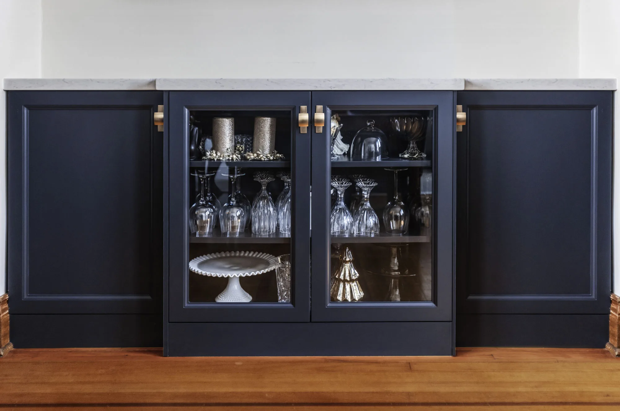 A close up of dark navy buffet with glass doors and gold hardware