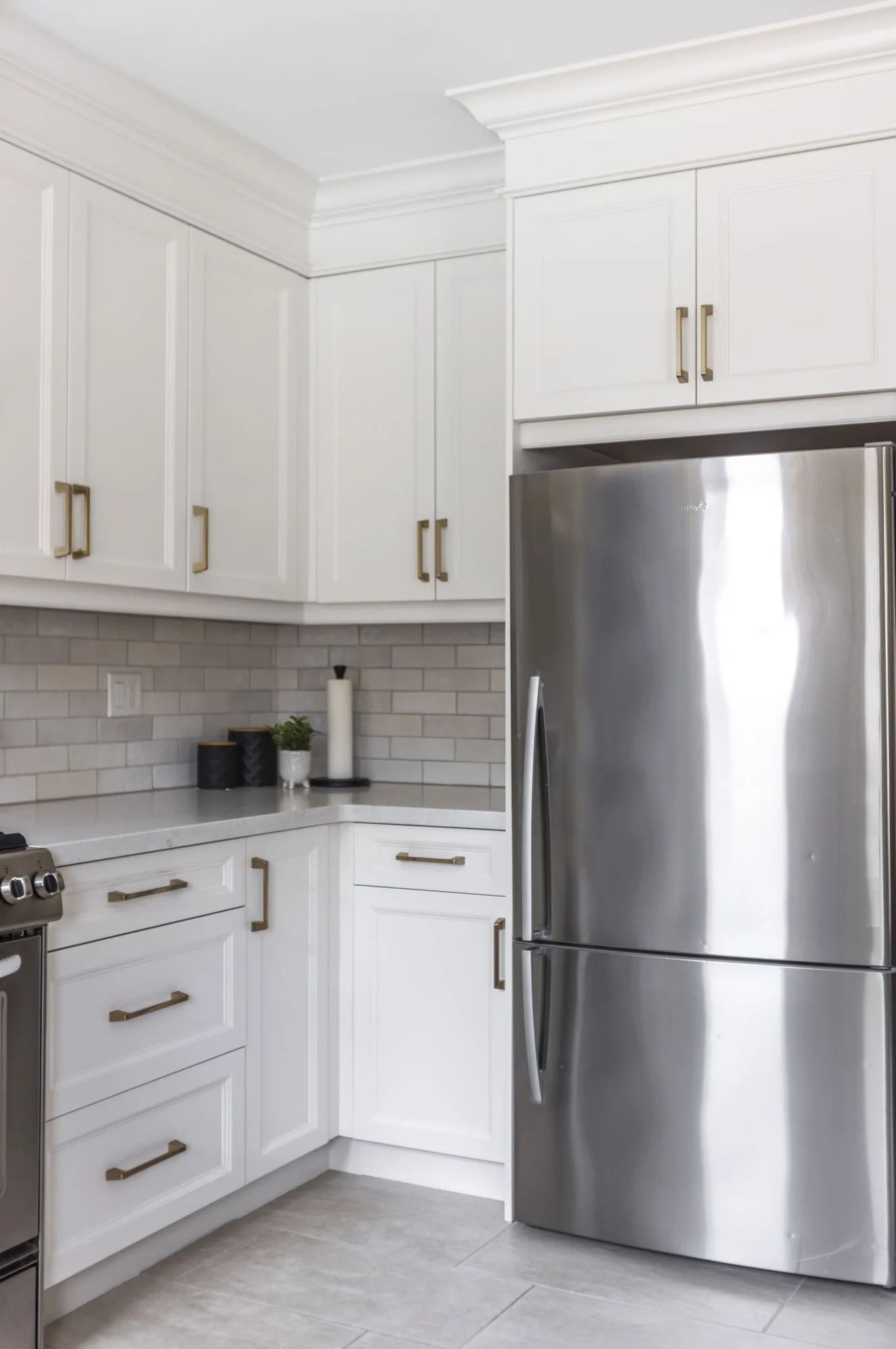 A kitchen with white upper and lower cupboards with silver handles with a stainless steel fridge.