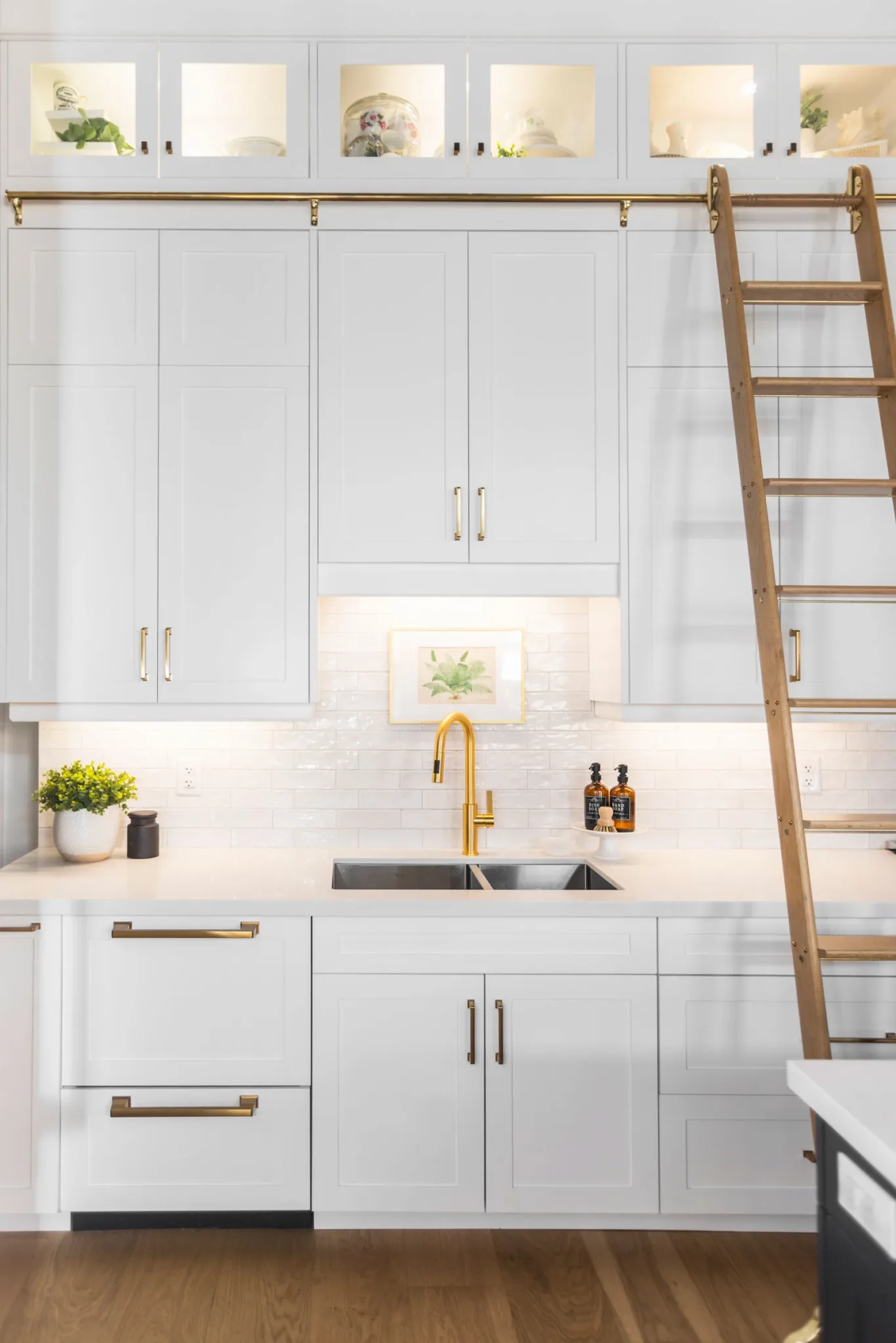 An all white modern kitchen with gold hardware with a gliding gold ladder