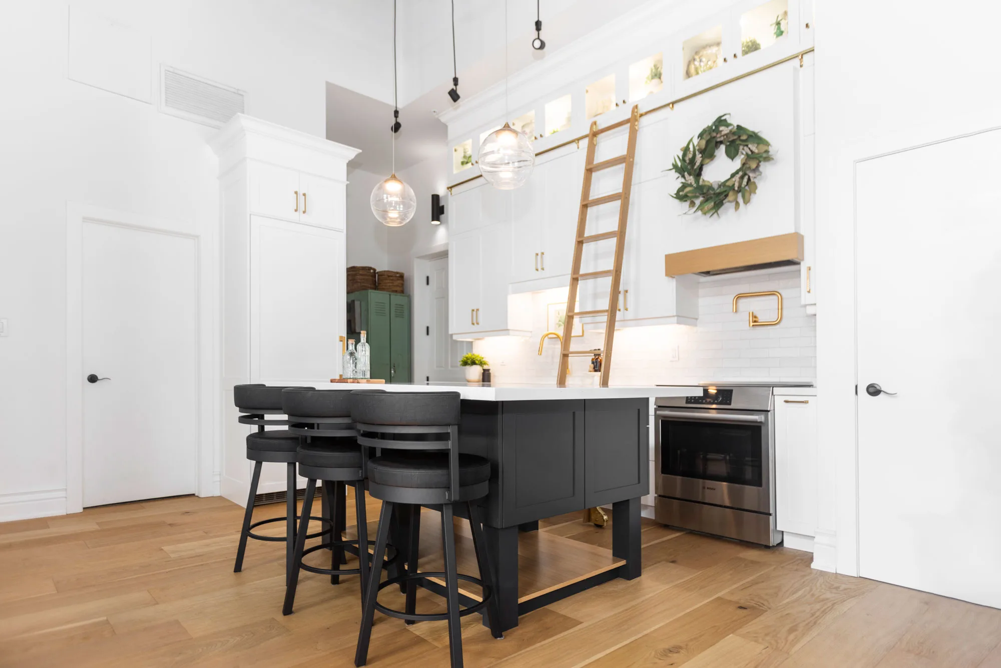An all white modern kitchen with gold hardware with a gliding gold ladder with a breakfast bar