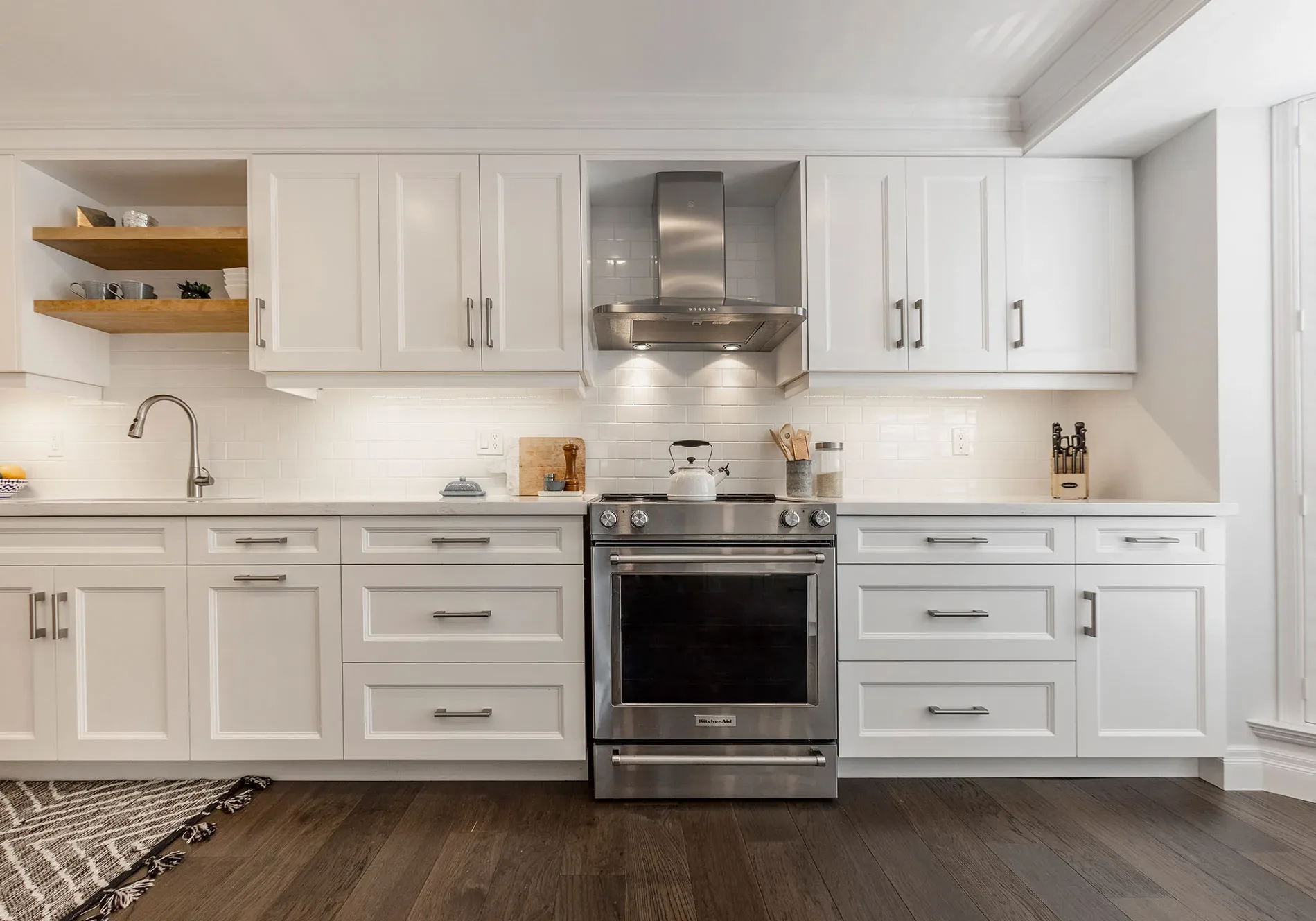 A modern kitchen with white cabinentry accented with silver handles and stainless steel stove and hood