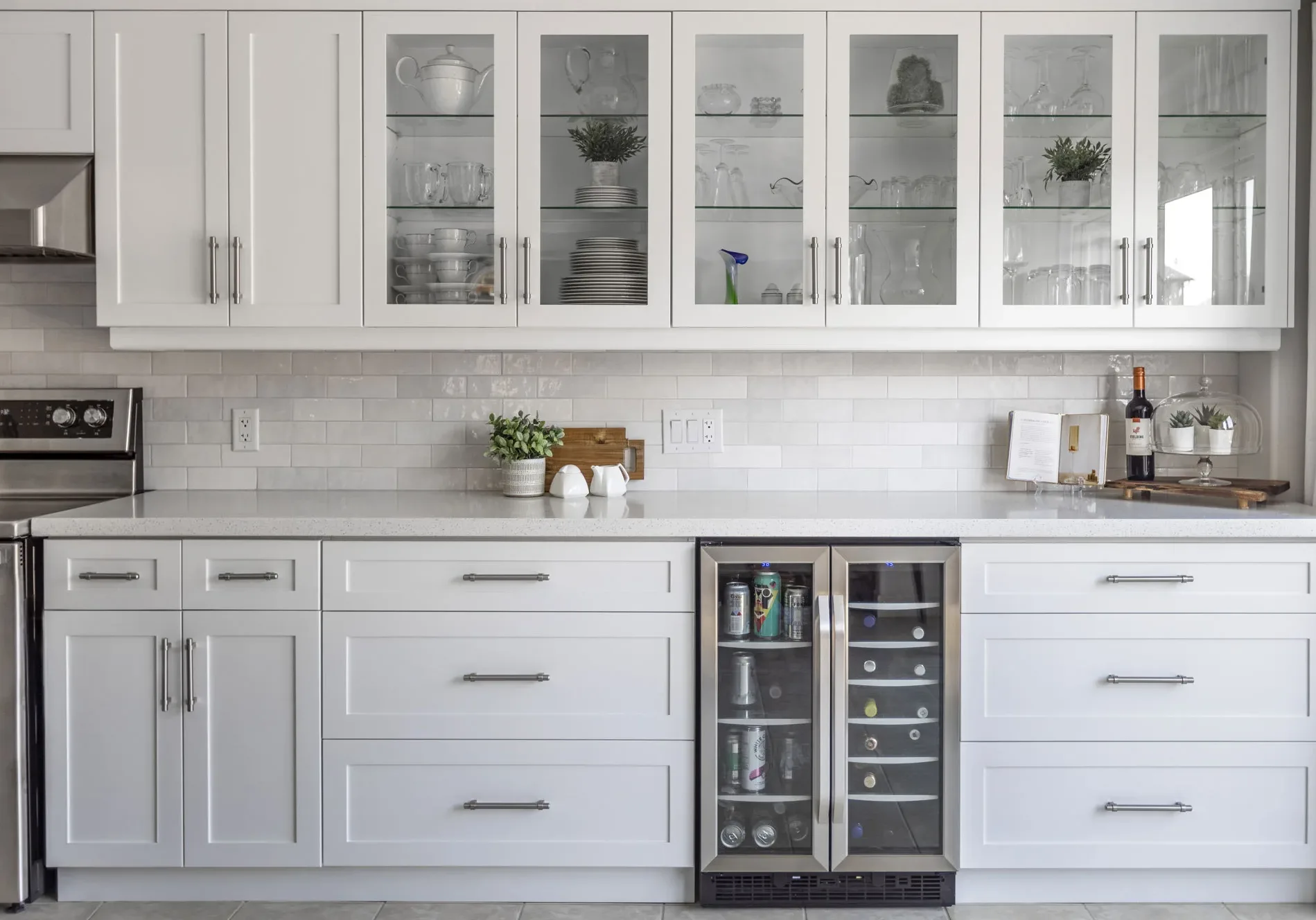 A modern white kitchen with glass top cupboards and a small stainless steel drink fridge.