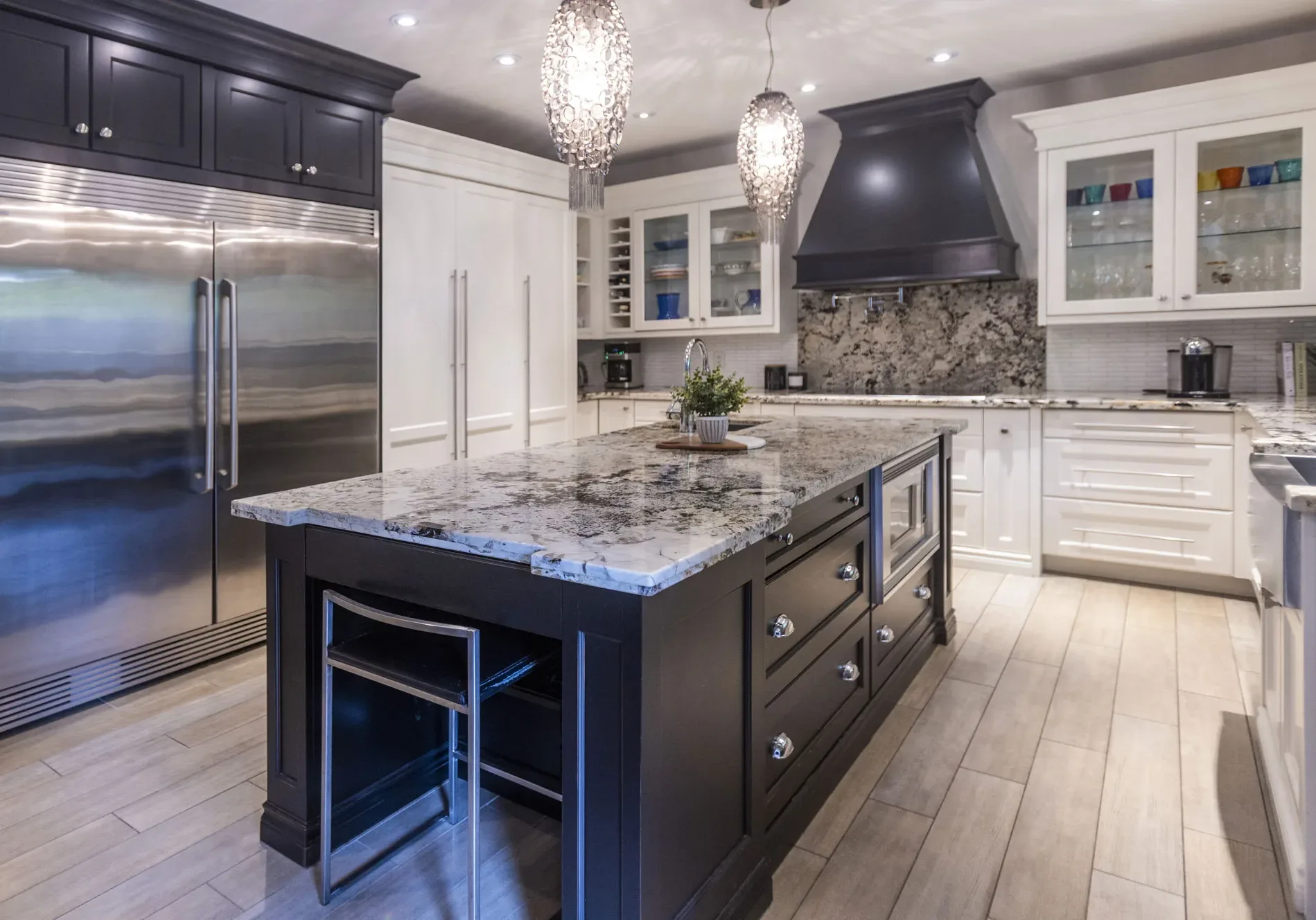 A kitchen with white cabinets and grey and black speckled granite counter top and back splash. Mixed with Dark blue cabinets with
