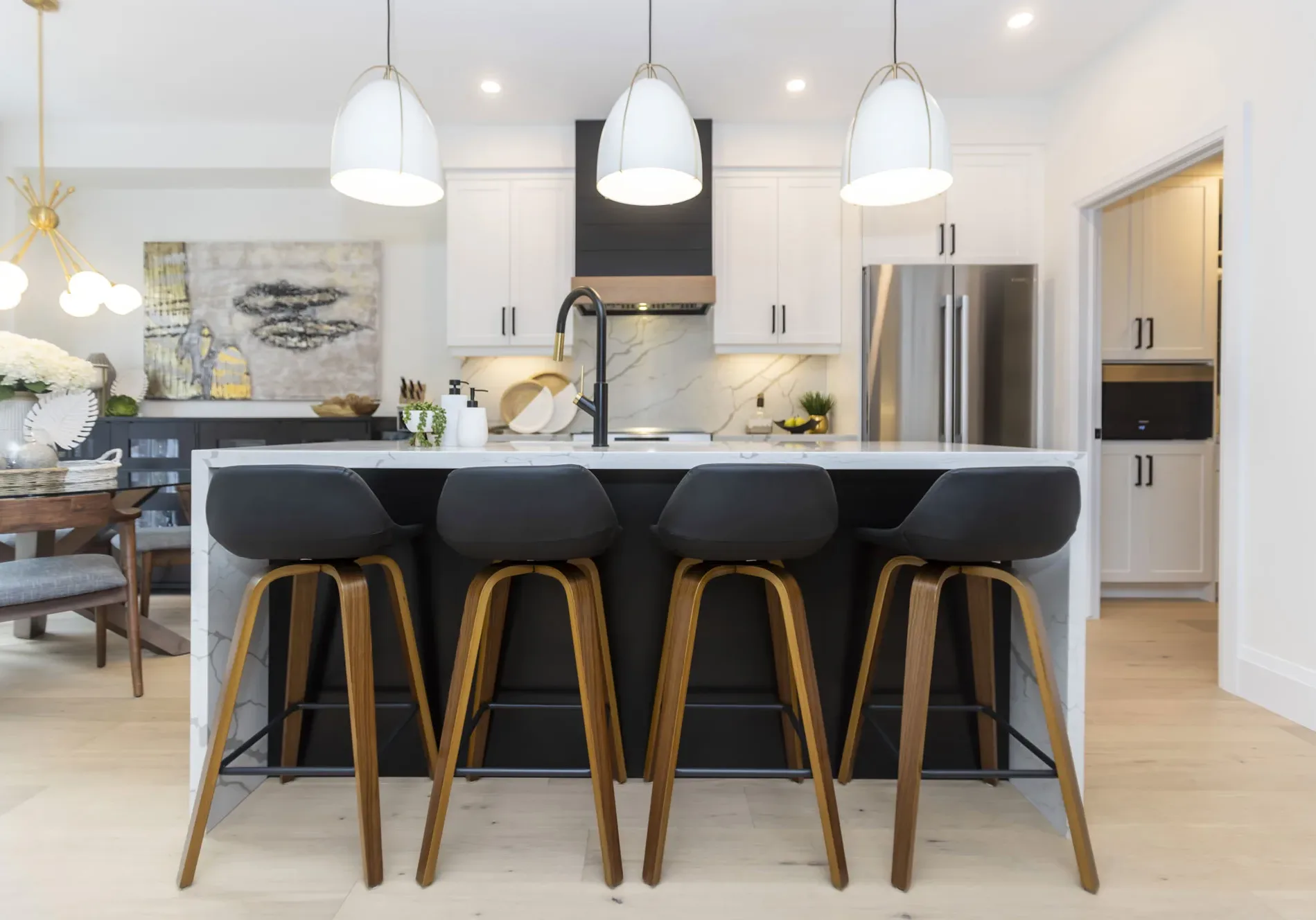 A modern kitchen with all white cabinets, black handles. An island with 4 modern black and wooden high top chairs