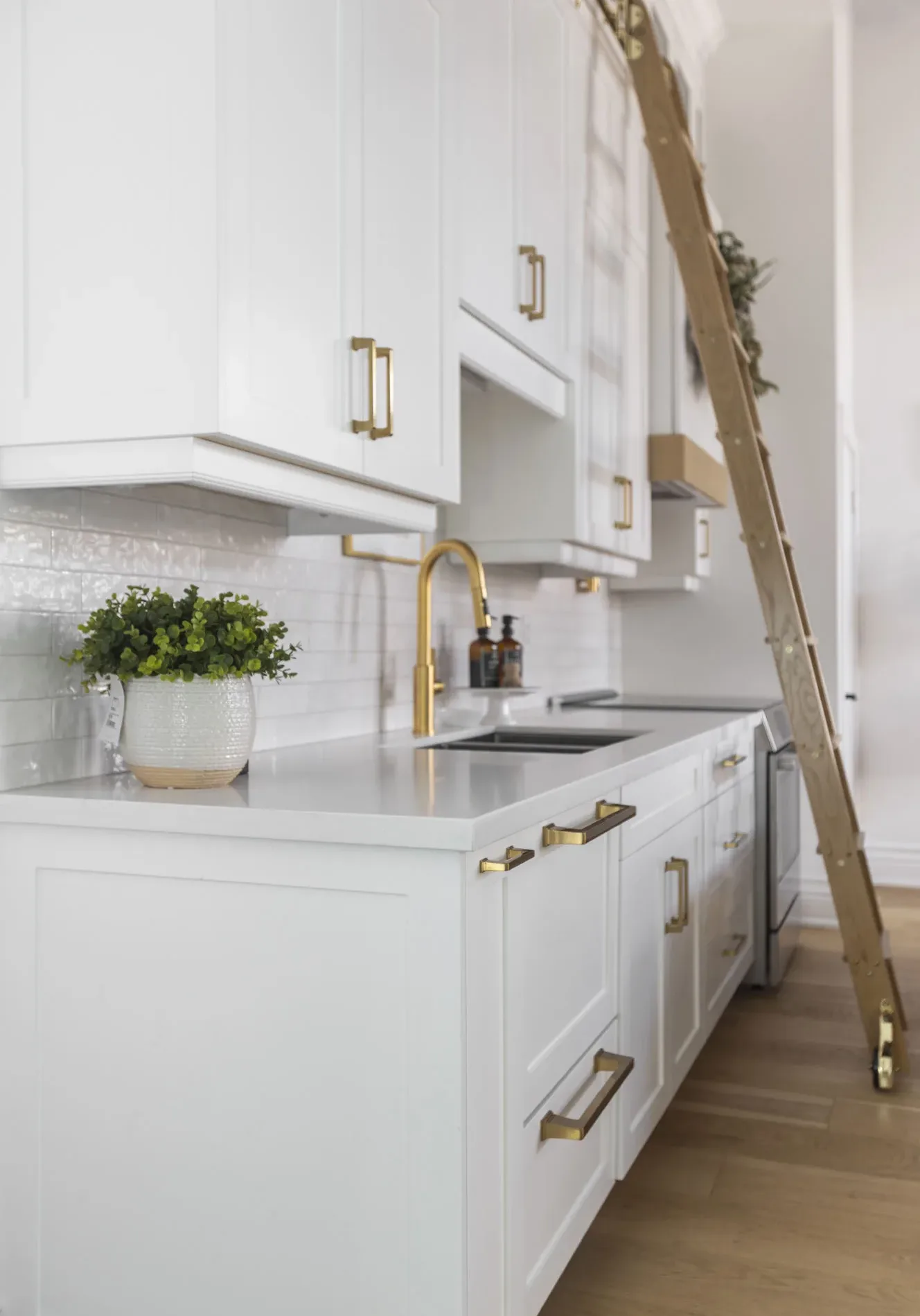 A side view of an all white modern kitchen with gold hardware with a gliding gold ladder