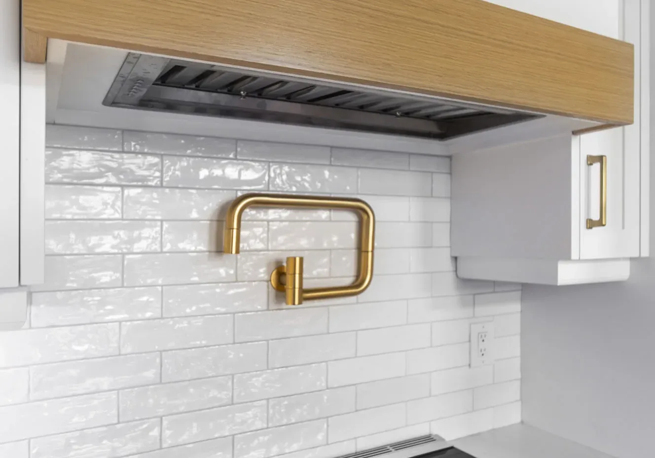 Close up a stove top with white back splash and gold water spout
