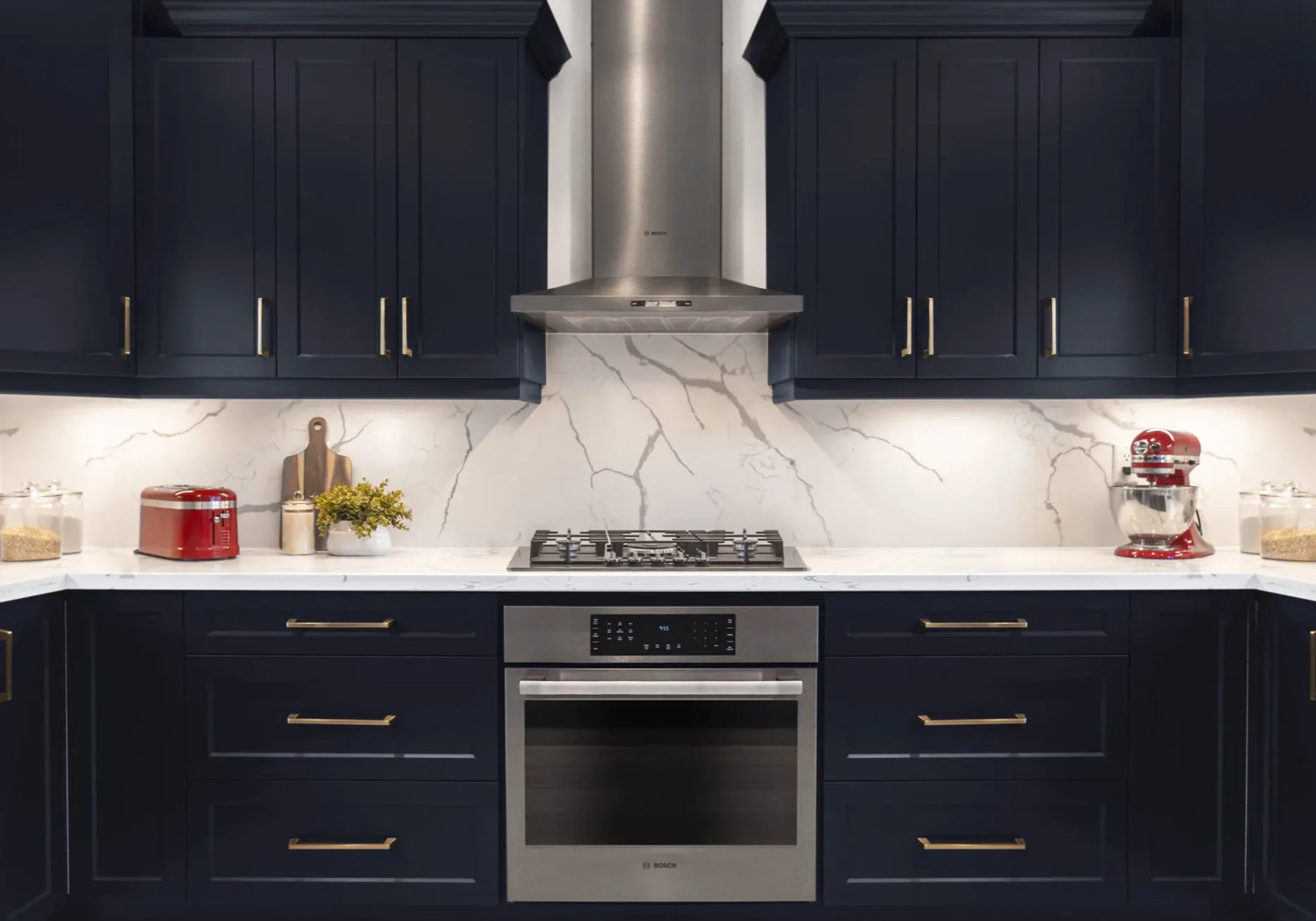 A a modern kitchen with dark blue cabinetry, silver handles, white counter tops and dark stainless steel stove.