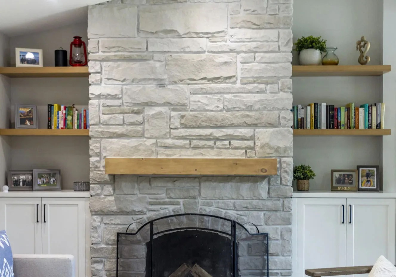 A light grey bricked fire place with a wooden fireplace with shelving on the left and right.